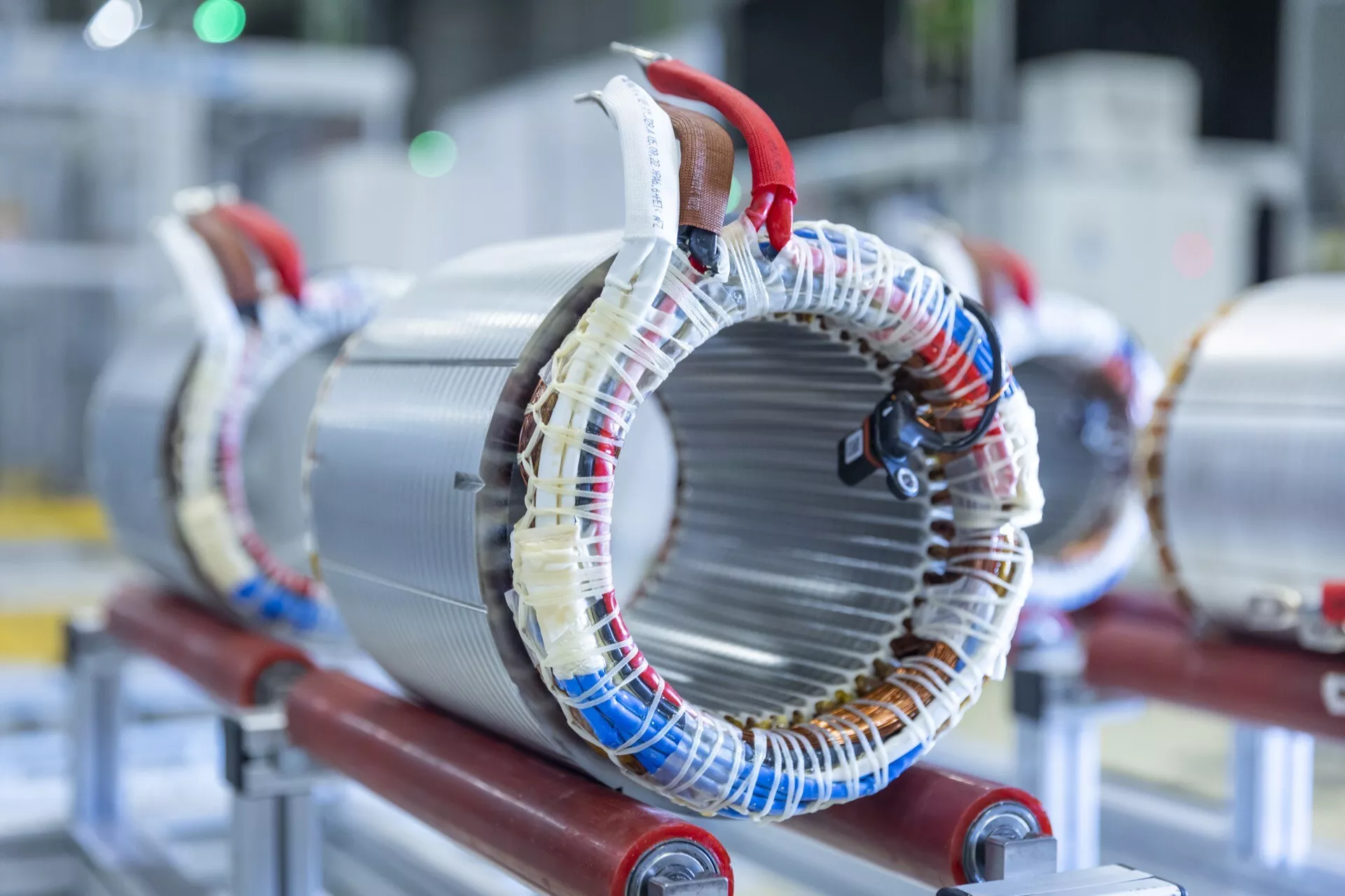 Foto de alta resolução de um estator de motor elétrico montado em suporte vermelho, mostrando bobinas de fio enroladas em torno de núcleos metálicos laminados típicos em maquinaria elétrica para gerar campos magnéticos