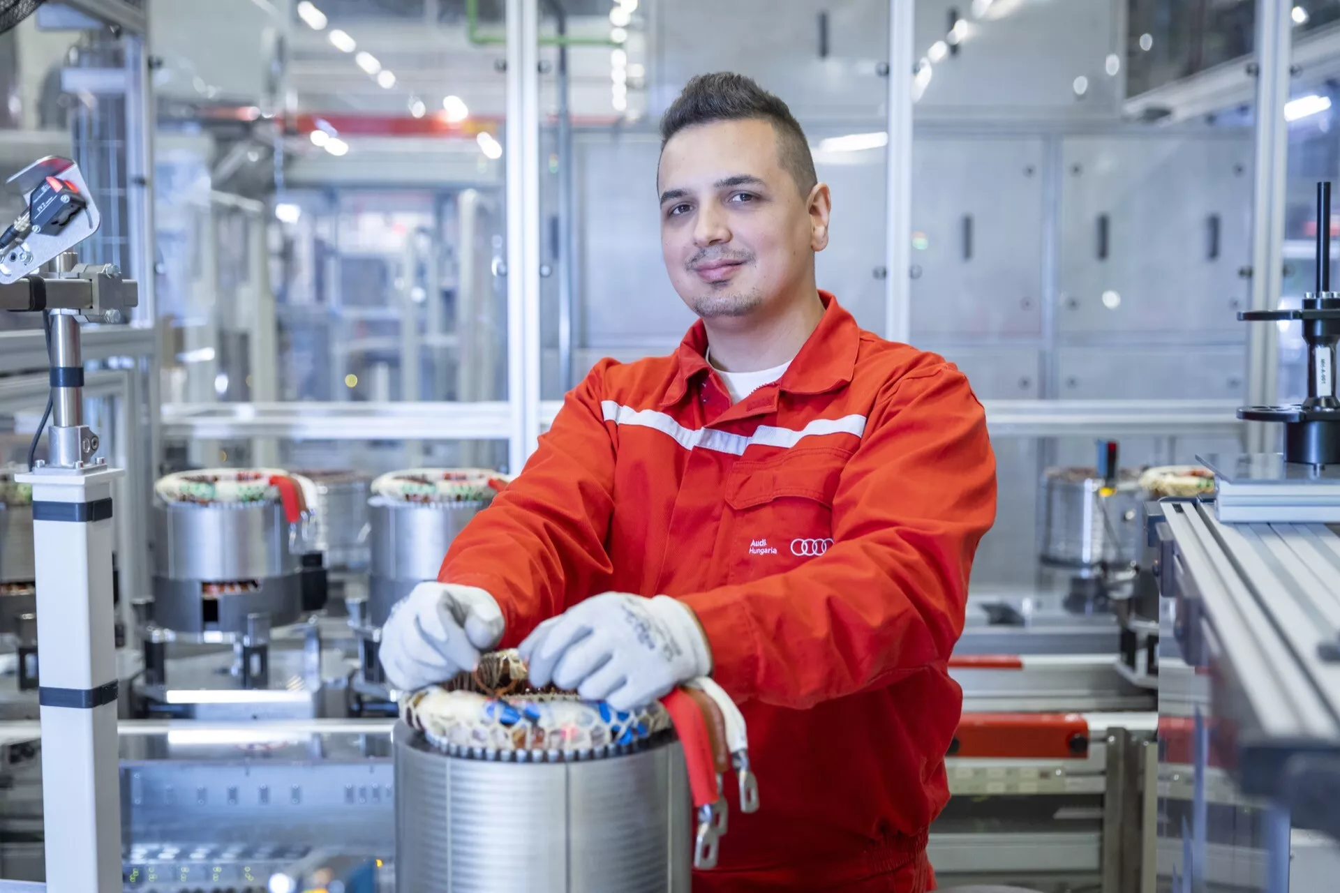 Profissional de engenharia automotiva em uniforme vermelho trabalhando em um componente de transmissão elétrica em uma instalação de fabricação moderna