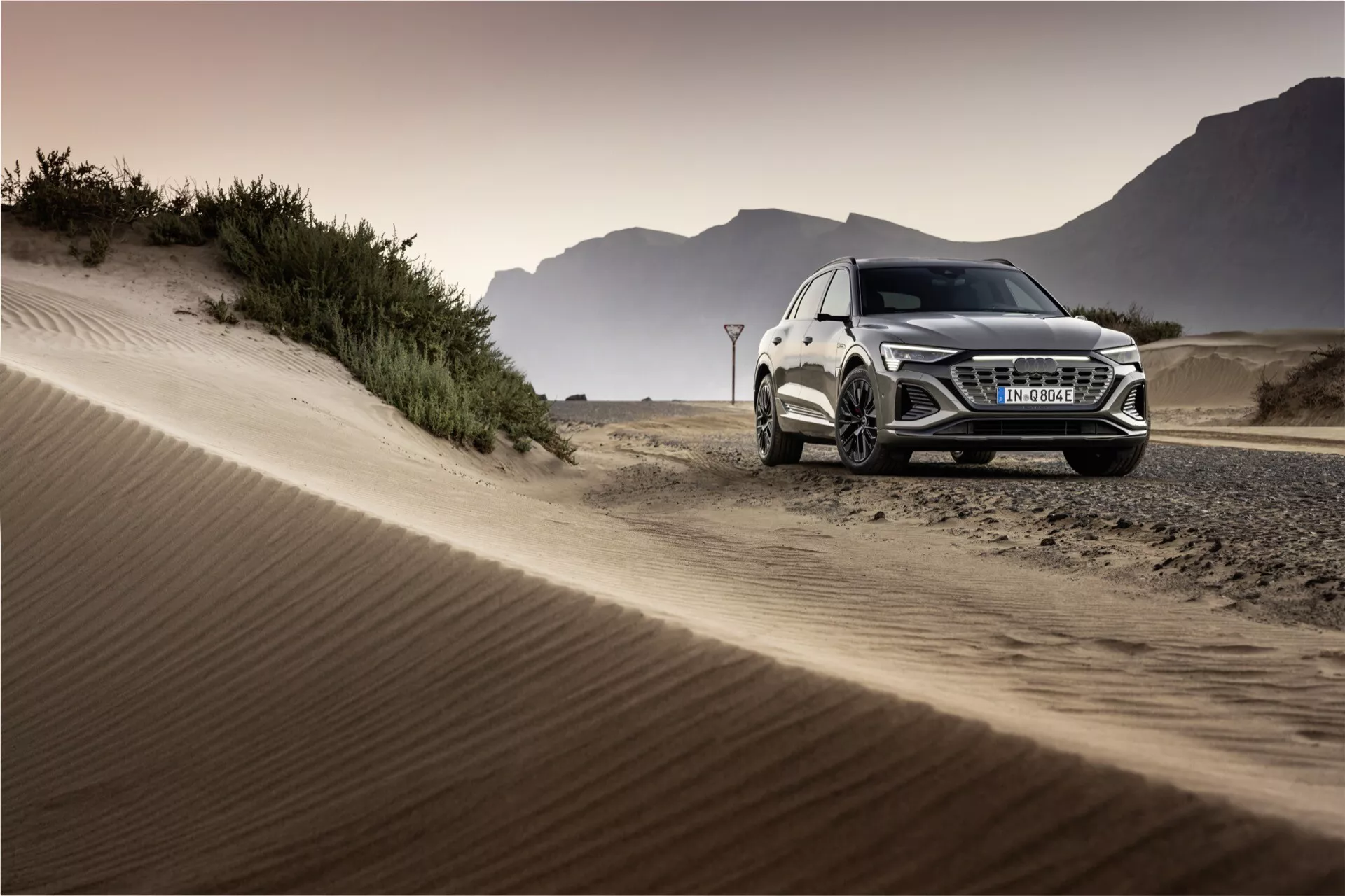 Audi Q8 e-tron 2023 em um cenário fora de estrada exibindo seu design de SUV de luxo, faróis LED, rodas de liga leve e capacidades de desempenho contra um pano de fundo de dunas de areia na hora dourada