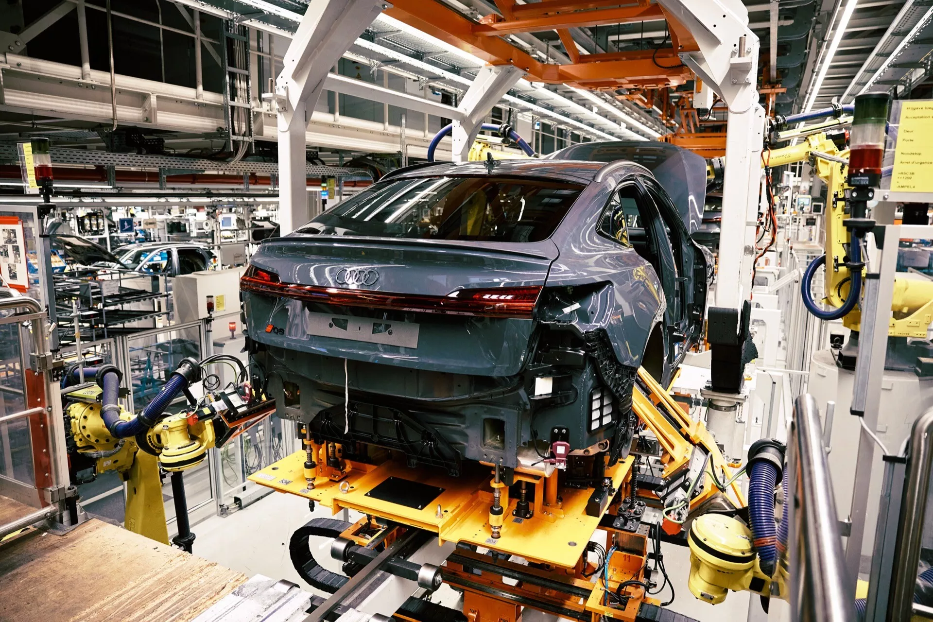 Audi Q8 e-tron 2023 em produção, vista traseira de três quartos destacando faróis traseiros LED e acabamento de alto brilho na linha de montagem