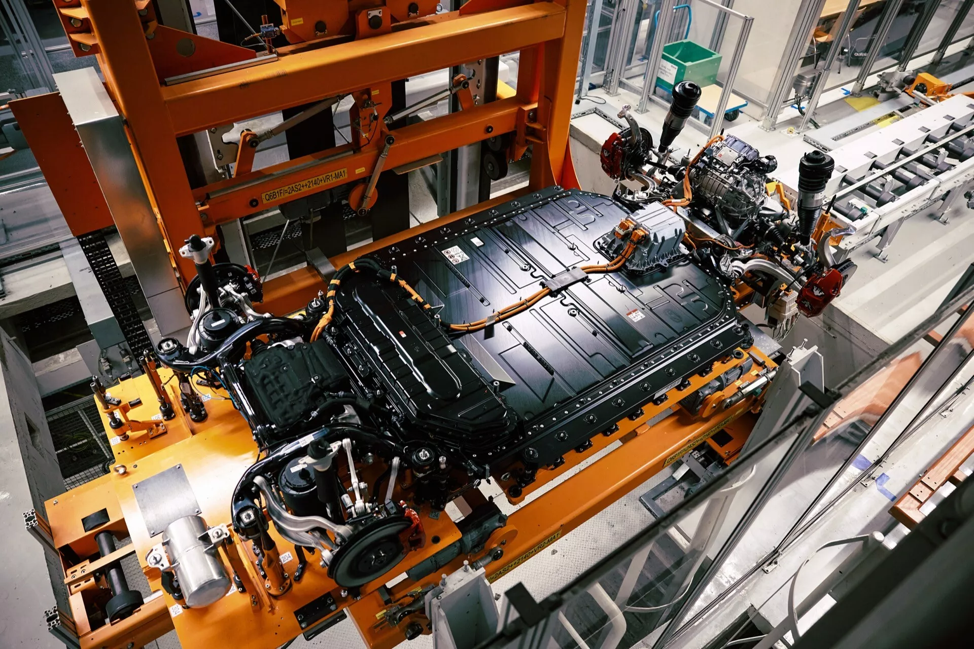 Vista de alto ângulo da parte inferior do Audi Q8 e-tron 2023 durante a montagem, mostrando o chassis, o grande pacote de bateria elétrica e o sistema de suspensão em um ambiente de fábrica