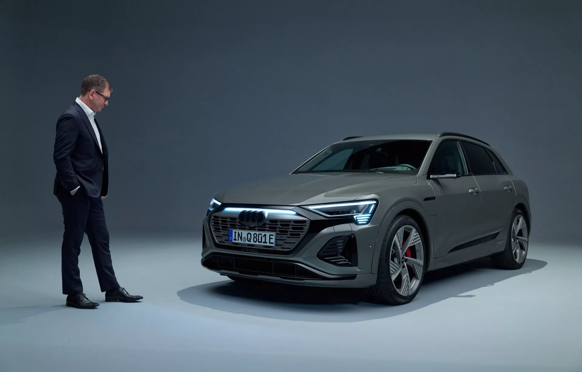 Audi Q8 e-tron 2023 em configuração de estúdio, mostrando um veículo elétrico de luxo moderno com design elegante, visto de uma perspectiva dianteira de três quartos de ângulo baixo contra um fundo de gradiente, com faróis LED completos e grandes rodas de liga leve