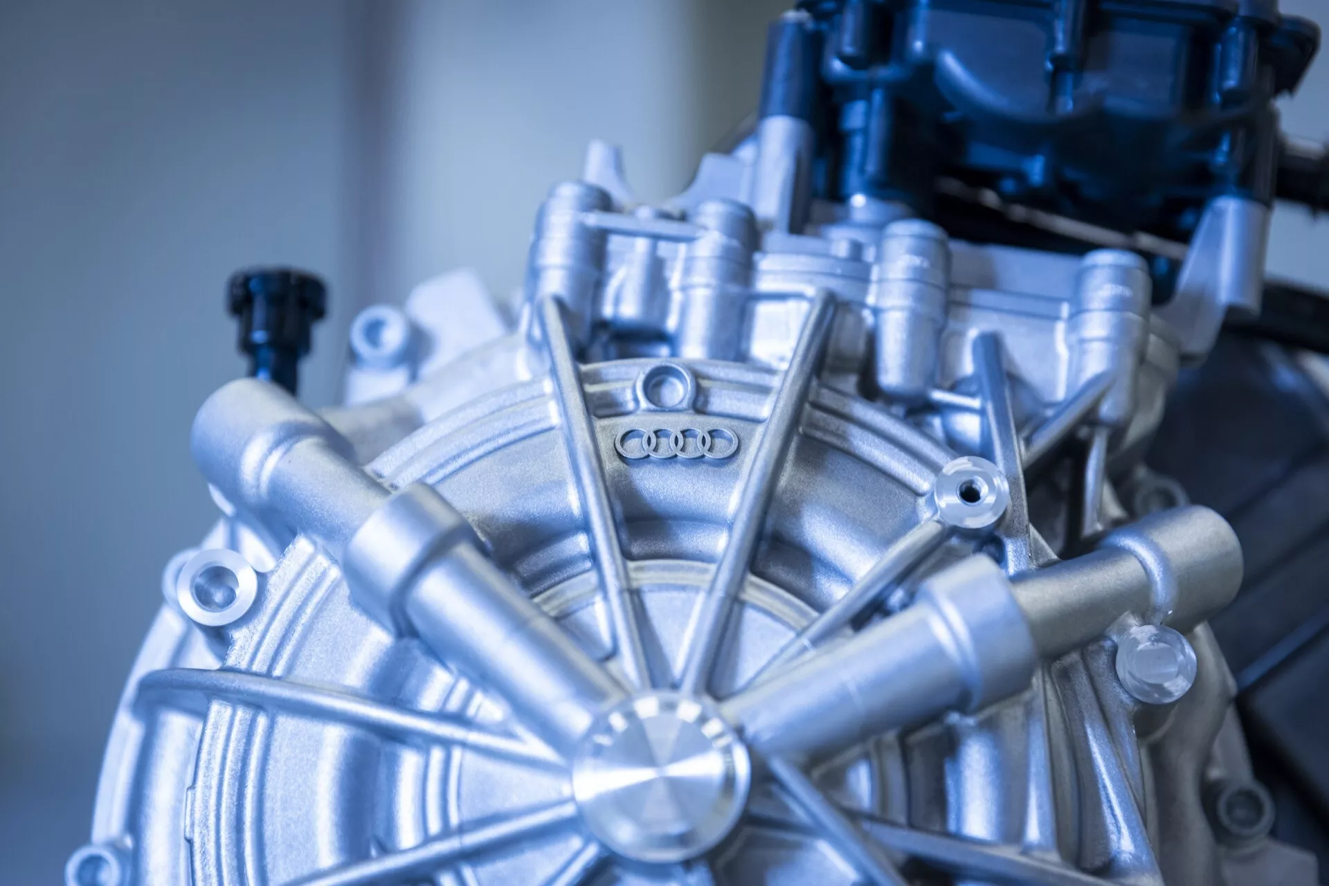 Vista detalhada do componente do motor do Audi Q8 e-tron 2023, apresentando o cubo circular com elementos radiantes e o logotipo da Audi, demonstrando a engenharia automotiva avançada e a fabricação de precisão.