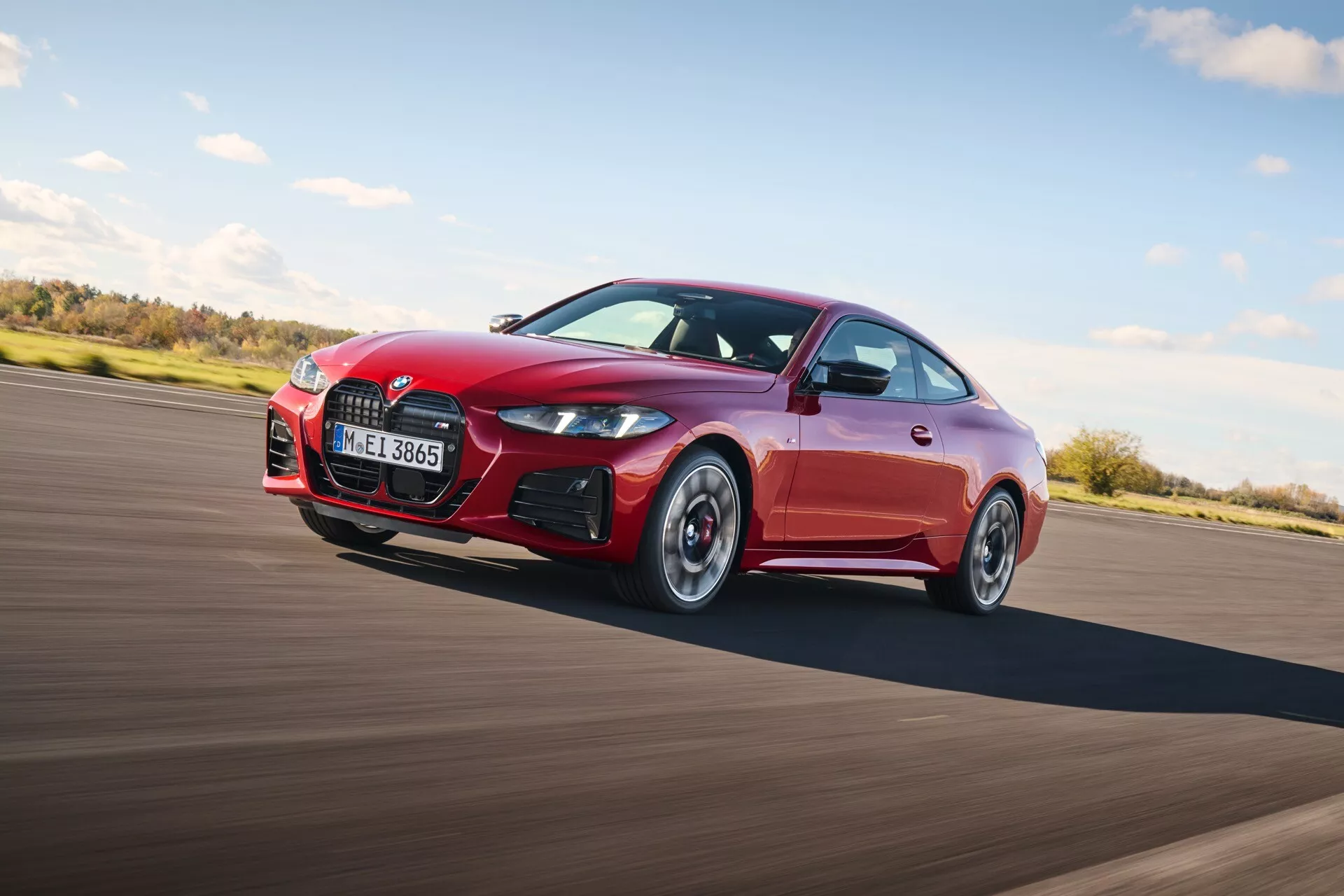 Vista dinâmica de um coupé esportivo vermelho da BMW Série 4 (G22-G23-G26-G82-G83 Facelift) em movimento, destacando o design elegante, grade frontal distintiva, para-choque esportivo com entradas de ar e características voltadas para o desempenho, capturada em um ângulo de 45 graus enfatizando o perfil aerodinâmico.