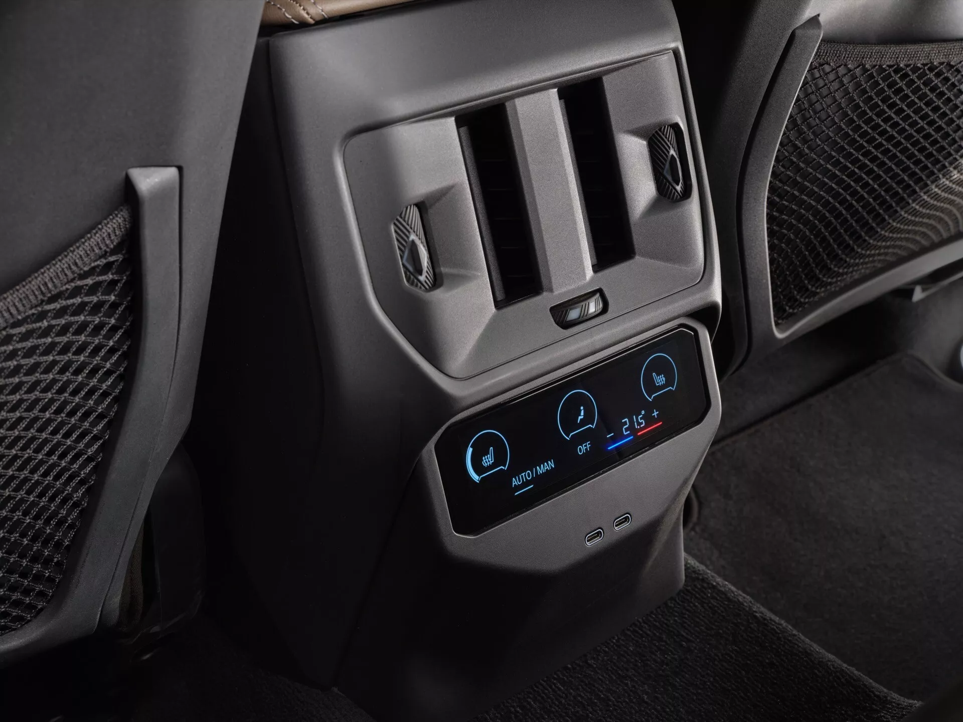 Imagem aproximada do sistema de controle climático traseiro do BMW X3 2024 (G45), focada no moderno painel digital com tela sensível ao toque retroiluminada em azul mostrando configurações de dupla zona a 22°C e 26°C, cercada por saídas de ar com acentos metálicos e ícones de aquecimento dos assentos, em um interior escuro de couro e plástico, destacando características avançadas de conforto e conveniência para os passageiros.