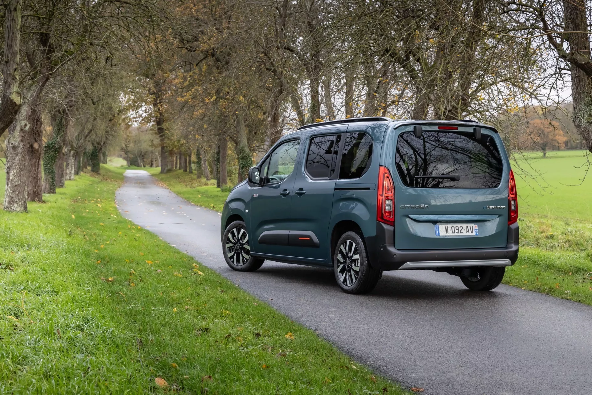Vista traseira de três quartos do Citroen Berlingo Facelift de 3ª geração 2024 em estrada rural, com placa ao estilo europeu, limpador de para-brisa traseiro e design moderno de luzes traseiras.