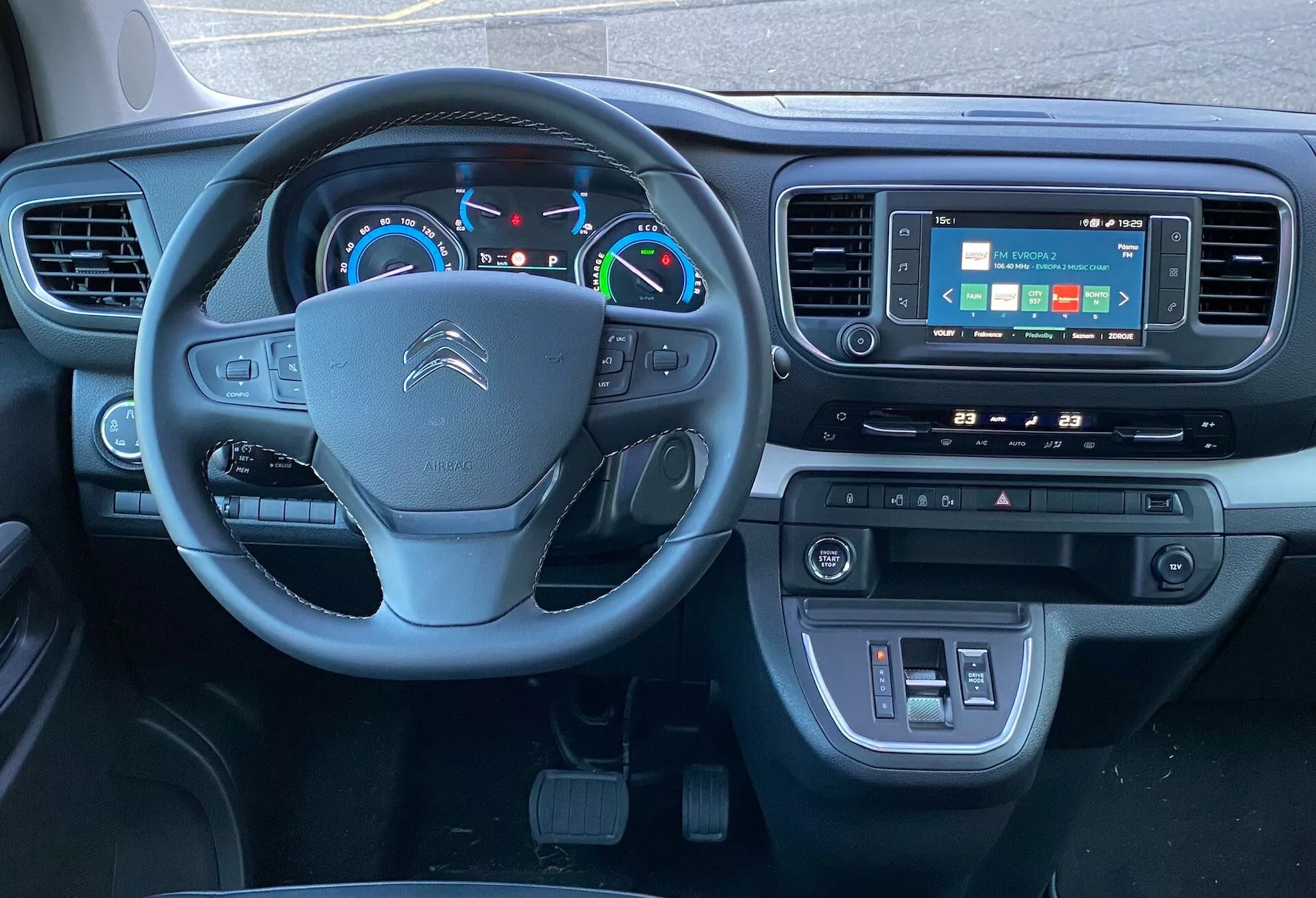 Vista interior do Citroën SpaceTourer 2016 a partir do banco do motorista, mostrando o volante com controles multifuncionais, painel de instrumentos digital e um sistema de infoentretenimento com tela sensível ao toque centralizado com controle de clima e conectividade USB abaixo. Ênfase na tecnologia e design moderno.