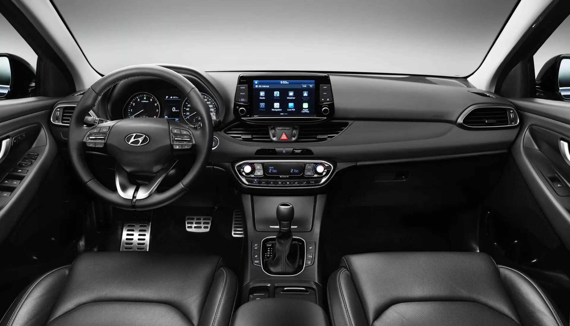 Interior do Hyundai i30 2017 Fastback mostrando o painel frontal a partir de uma perspectiva do banco traseiro, com volante posicionado no centro para a esquerda com botões de controle e logotipo da Hyundai, um cluster de instrumentos digital atrás, um grande sistema de infotenimento com tela sensível ao toque com aplicativos de conectividade, controle climático de zona dupla, alavanca de transmissão automática, controles potenciais para aquecimento/arrefecimento dos assentos e assentos revestidos em couro.