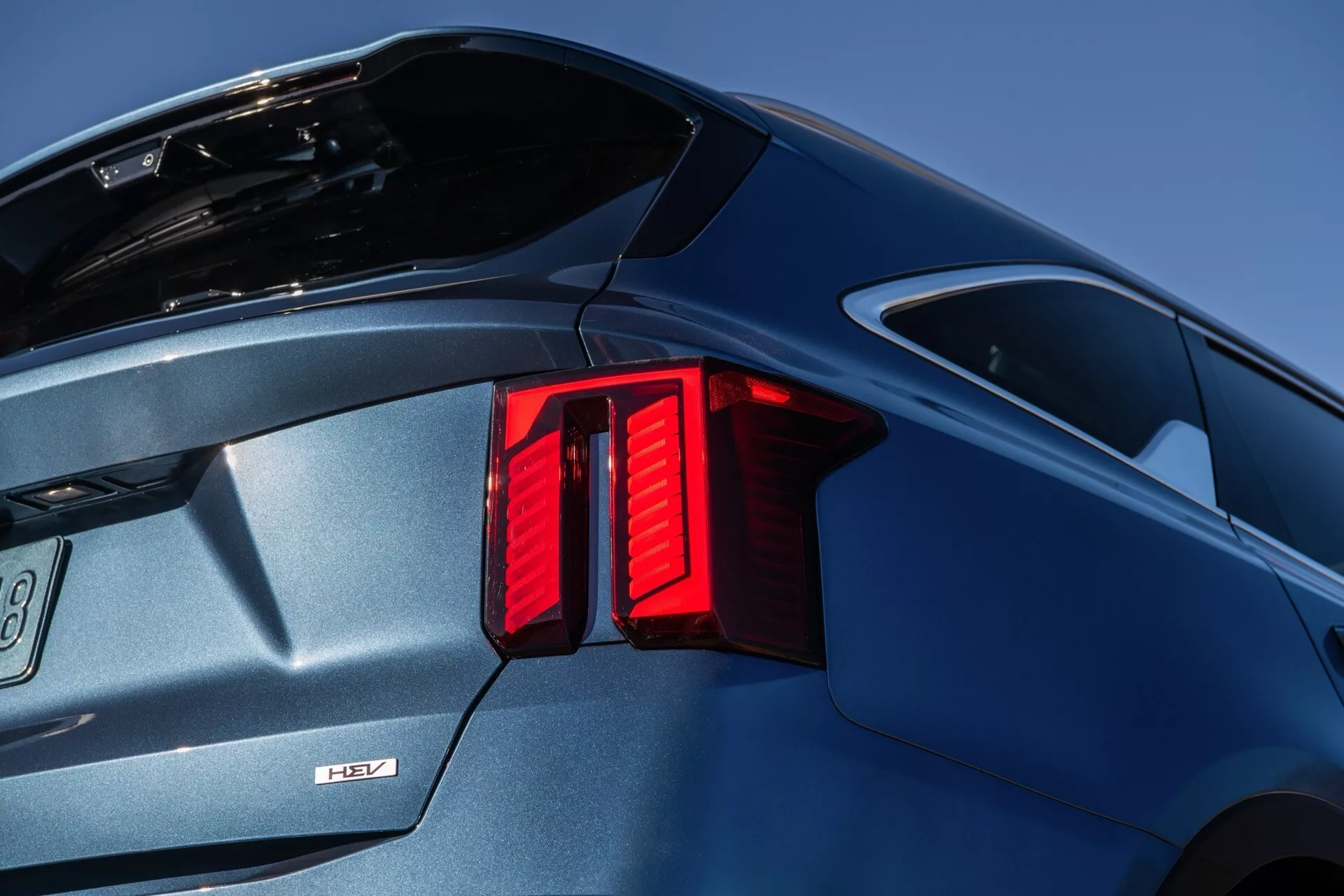 Facelift do Kia Sorento MQ4 2024 destacando o design moderno das luzes traseiras LED verticais, spoiler integrado ao porta-malas para melhor aerodinâmica, para-choque traseiro esculpido e acabamento metálico azul brilhante contra um fundo de céu azul claro