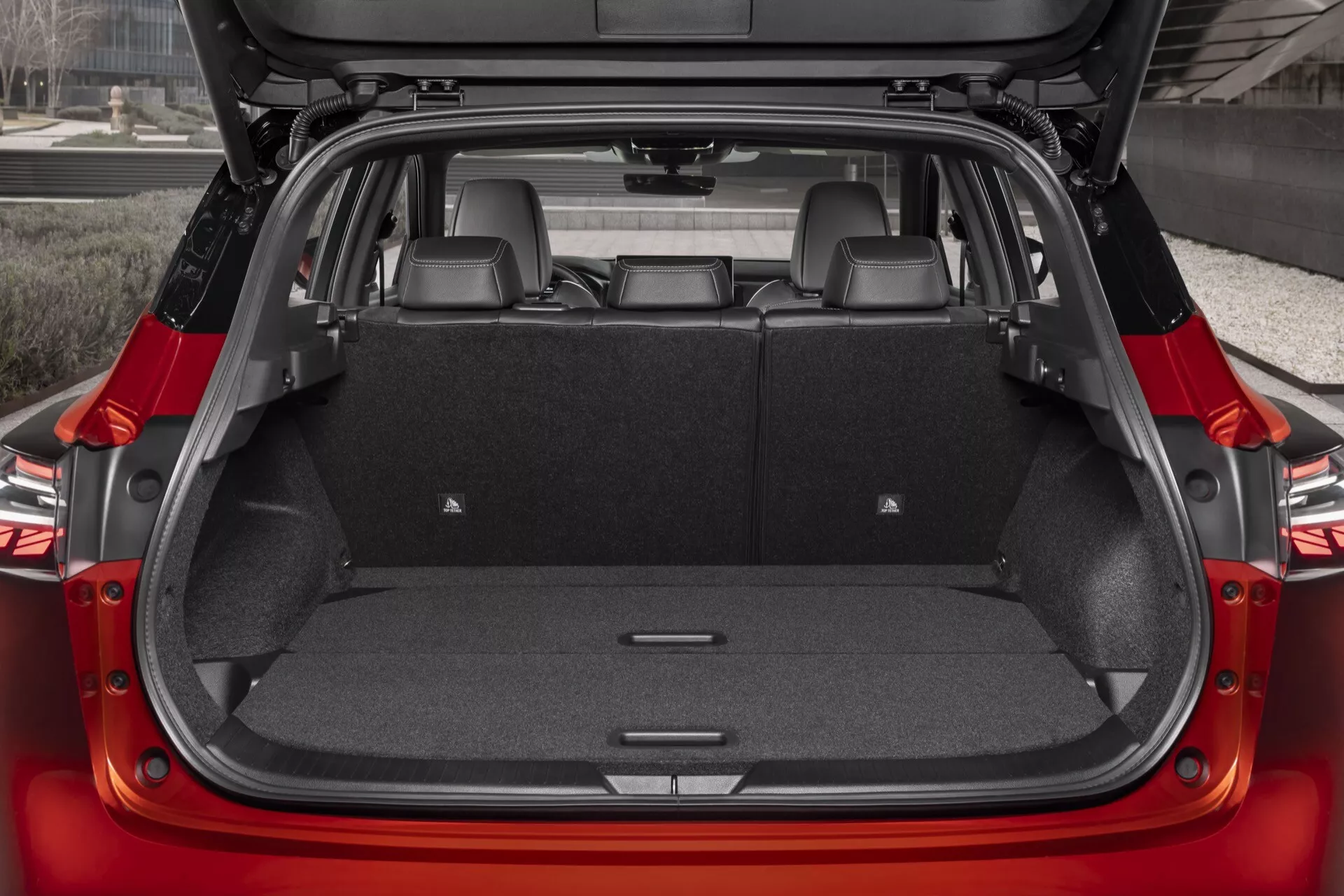 Vista detalhada do interior do porta-malas de um Nissan Qashqai 2024 (J12-facelift) com a tampa traseira aberta, mostrando uma área de carga espaçosa com os assentos na posição vertical e capacidade de rebatimento dividido 60/40. Revestimento em carpete escuro, pequenos compartimentos laterais e pontos de amarração visíveis. Imagem de alta qualidade destacando o espaço do porta-malas e as possíveis características de conveniência.