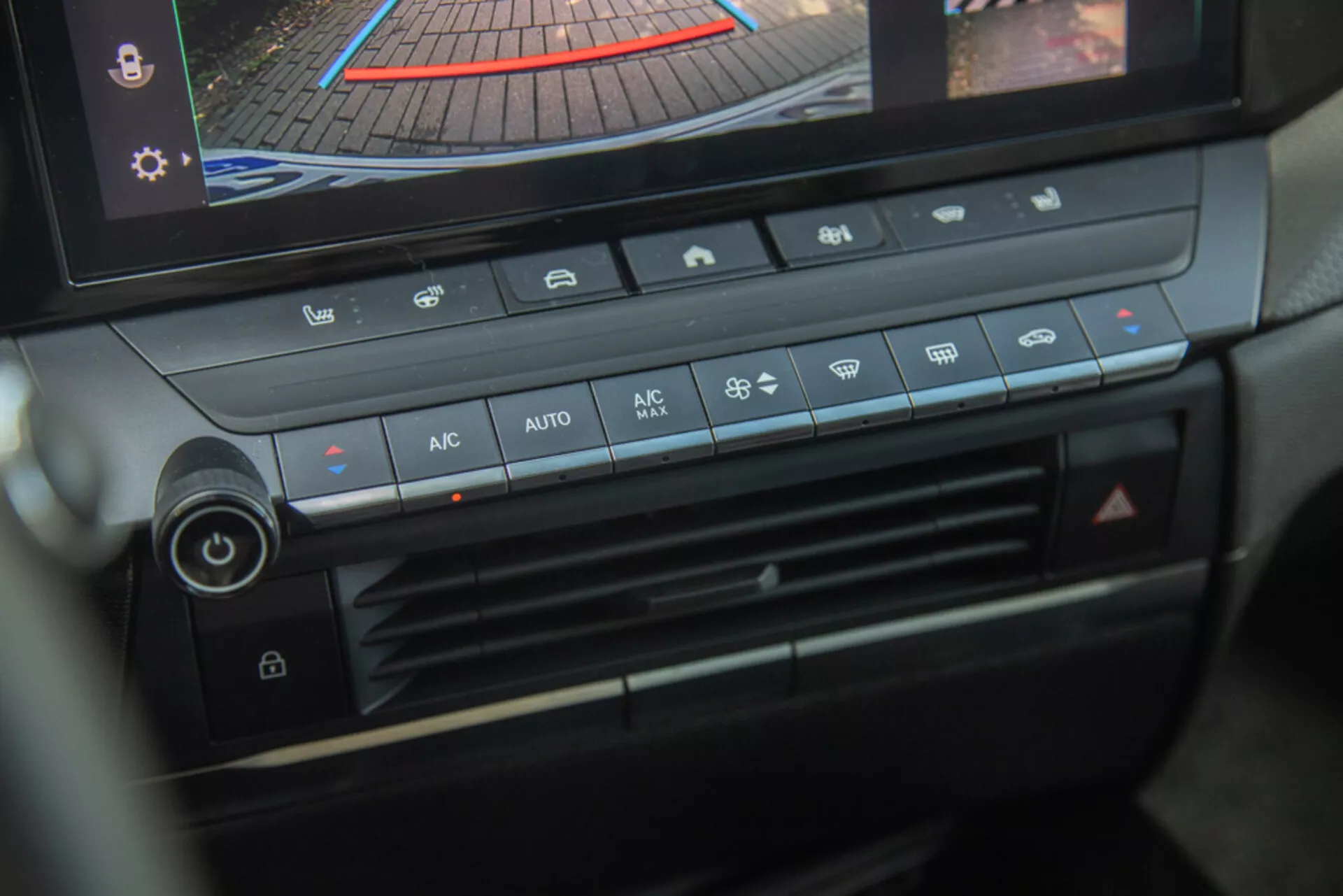 Console central e painel de controlo climatérico do Opel Astra 2022, destacando o botão de ajuste de temperatura, velocidade do ventilador, distribuição de ar e botões de controlo climático automático com display digital mostrando câmara traseira