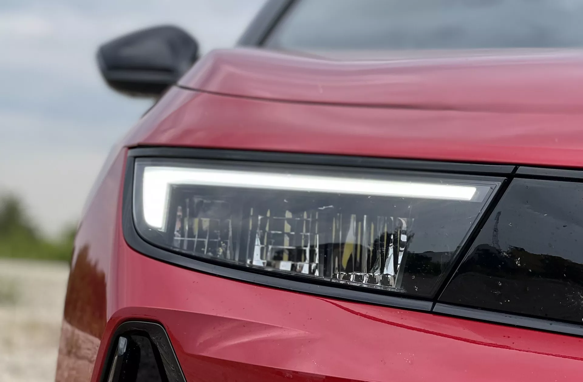 Vista frontal lateral em close-up de um Opel Astra vermelho de 2022 focando no design detalhado do farol LED, exibindo a tecnologia de iluminação moderna e os contornos do veículo