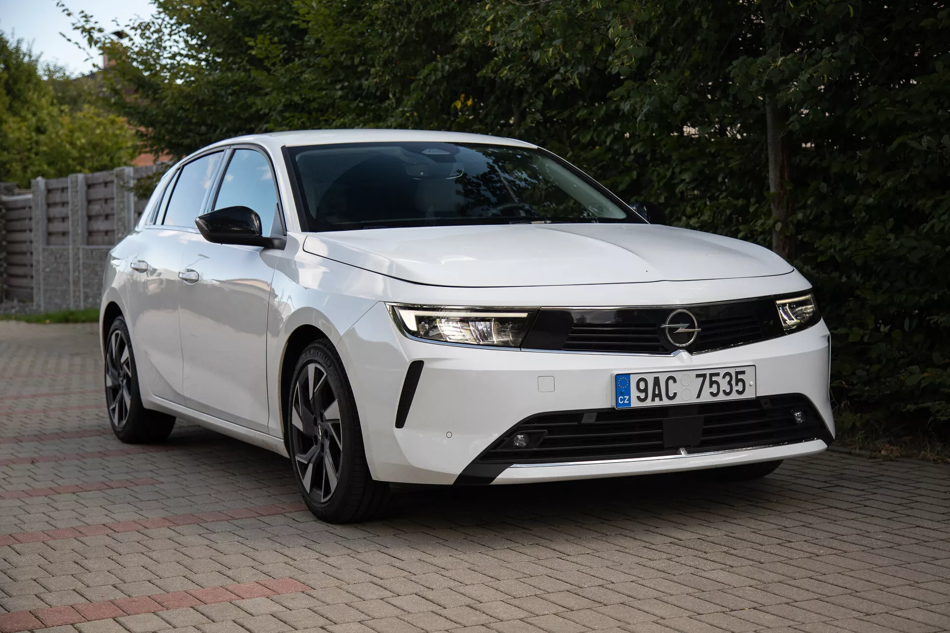 Opel Astra 2022 capturado num cenário suburbano, exibindo seus faróis elegantes, grelha frontal proeminente, design aerodinâmico incluindo rodas de liga leve de múltiplos raios, e tecnologia inovadora a partir de uma vista frontal de três quartos