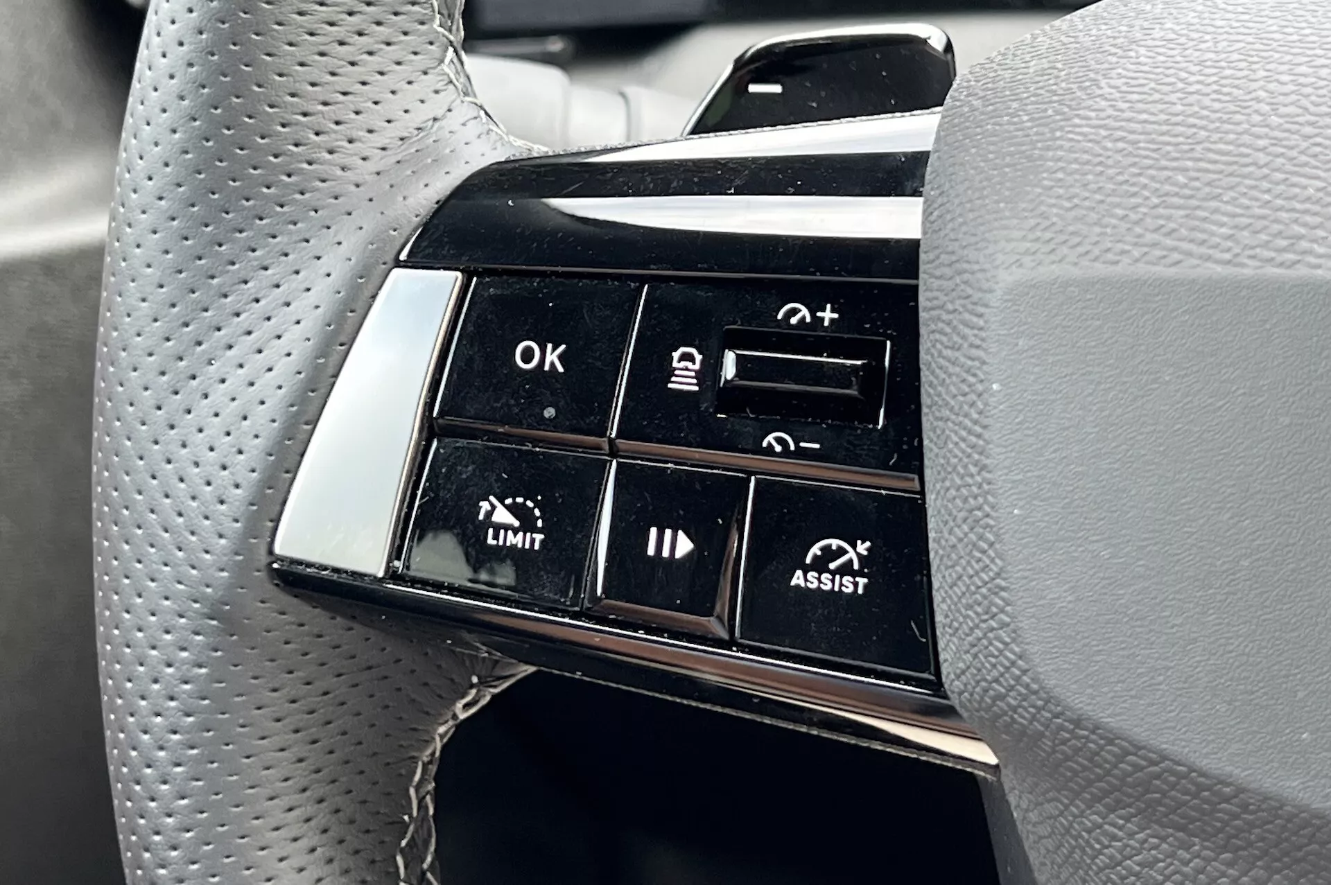 Visão detalhada do agrupamento de botões no volante do Opel Astra 2022 destacando recursos avançados de assistência à condução, incluindo controle de cruzeiro adaptativo e assistência de manutenção de faixa, com foco em rótulos de funcionalidade como OK, +, -, LIMIT e ASSIST na perspectiva do motorista