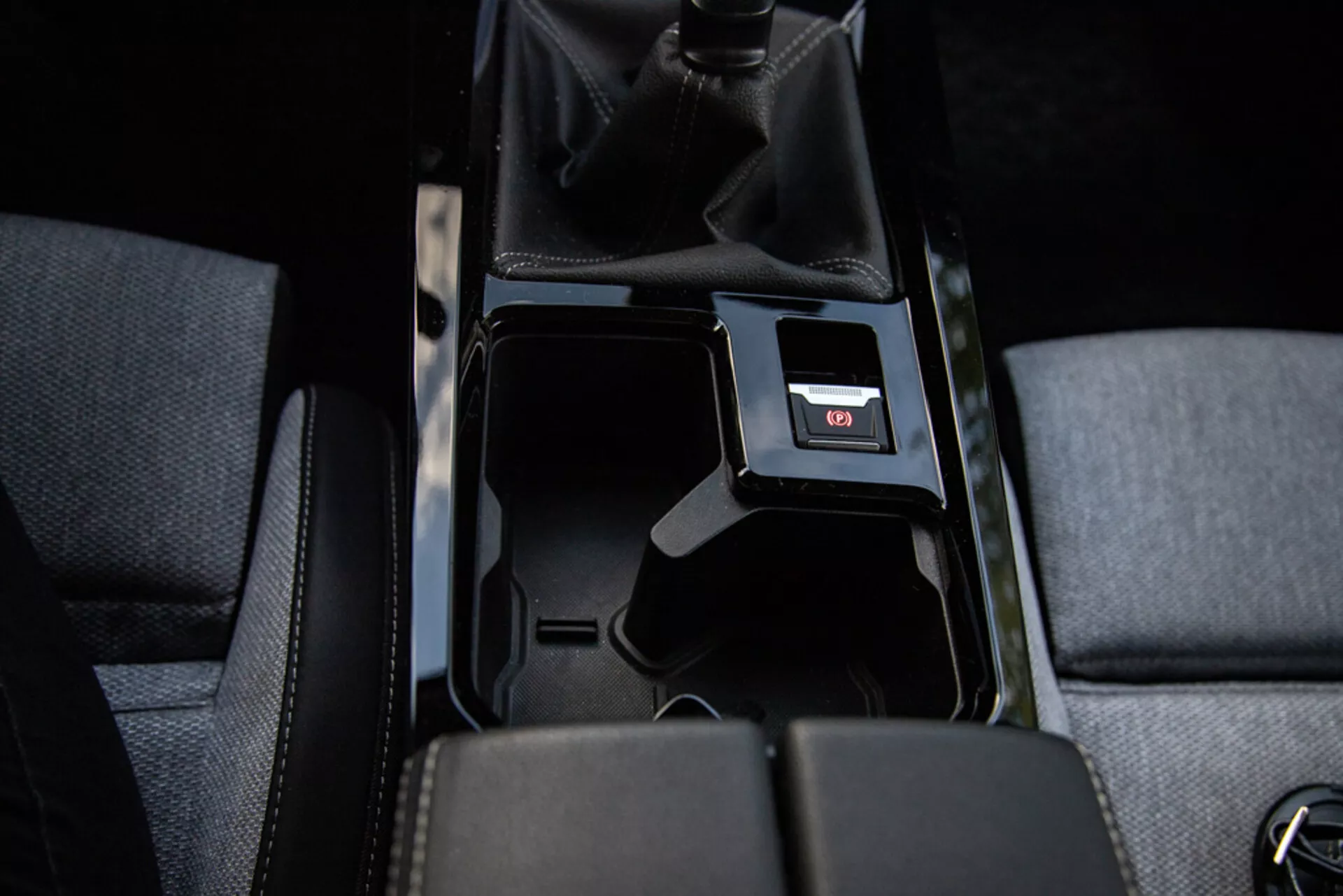 Detalhe do console central do Opel Astra 2022 mostrando compartimento de armazenamento aberto, estofamento de tecido, alavanca de câmbio manual com couro perfurado, porta USB e iluminação interna