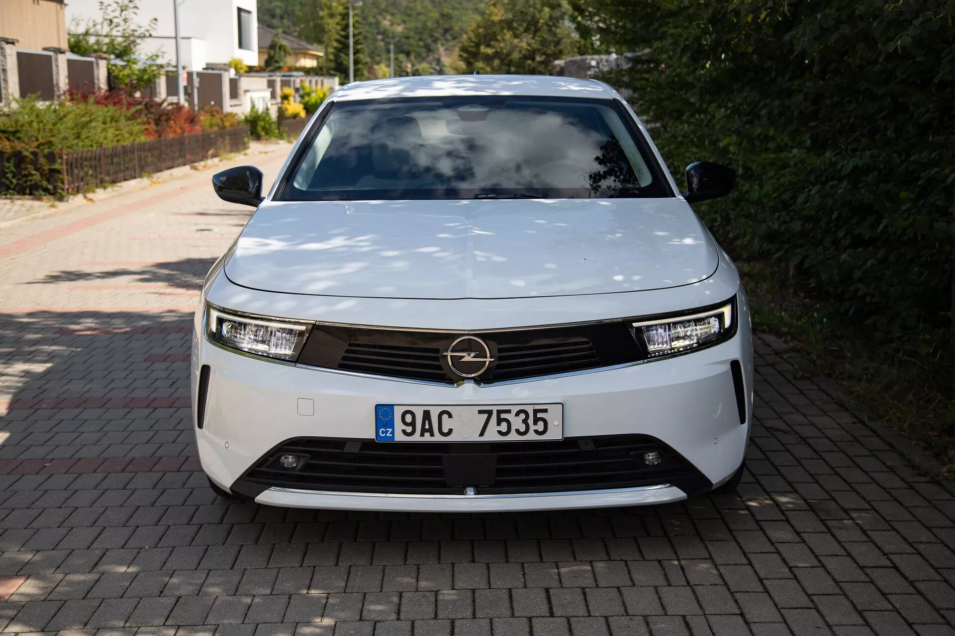 Vista frontal do Opel Astra 2022 exibindo um design moderno de veículo elétrico com faróis LED, grade decorativa e forma aerodinâmica, estacionado em uma entrada de residência