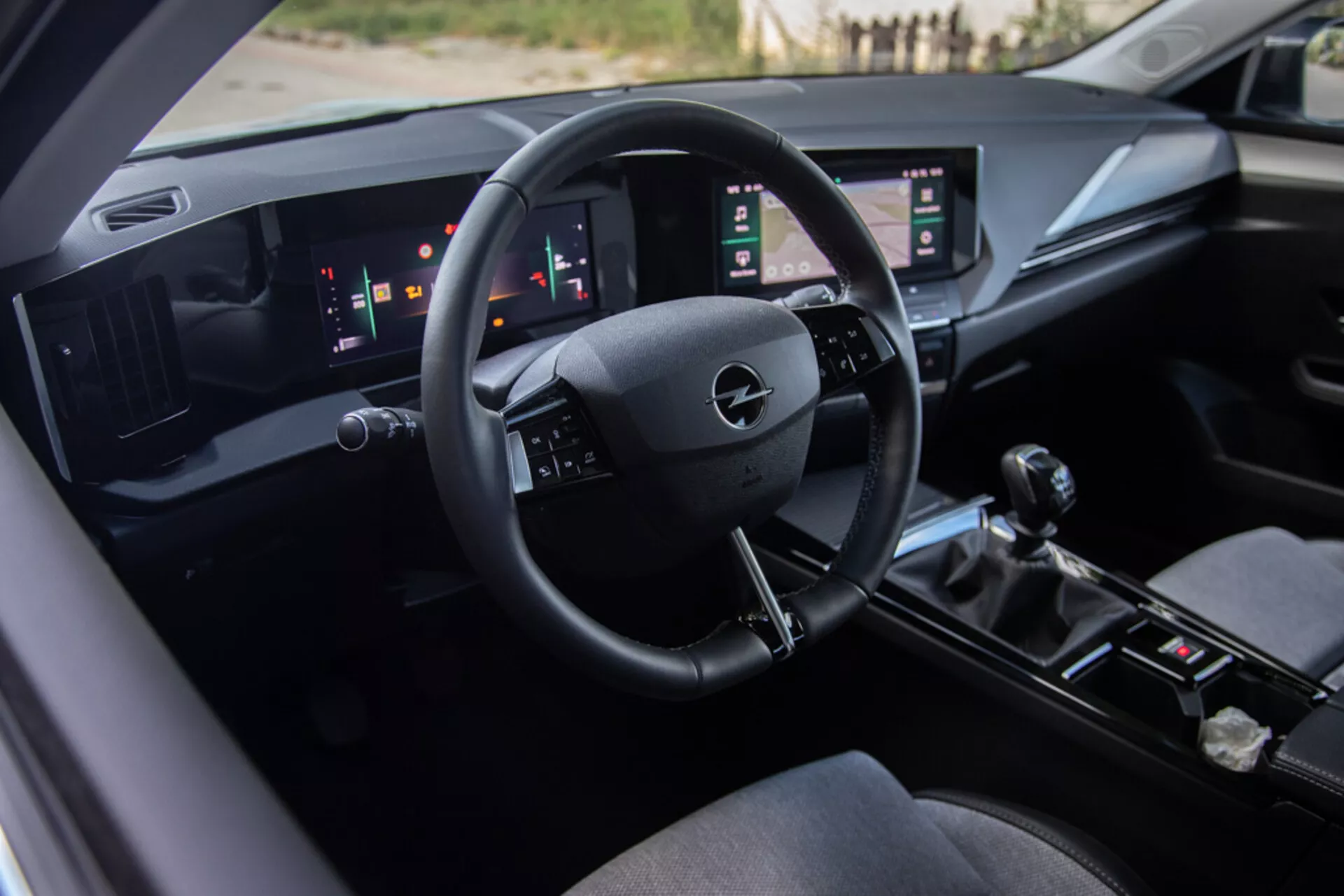 Interior do Opel Astra 2022 destacando o assento do motorista, um painel de bordo tecnologicamente avançado com o logotipo da Opel no volante, indicadores digitais e painéis touchscreen verticais duplos