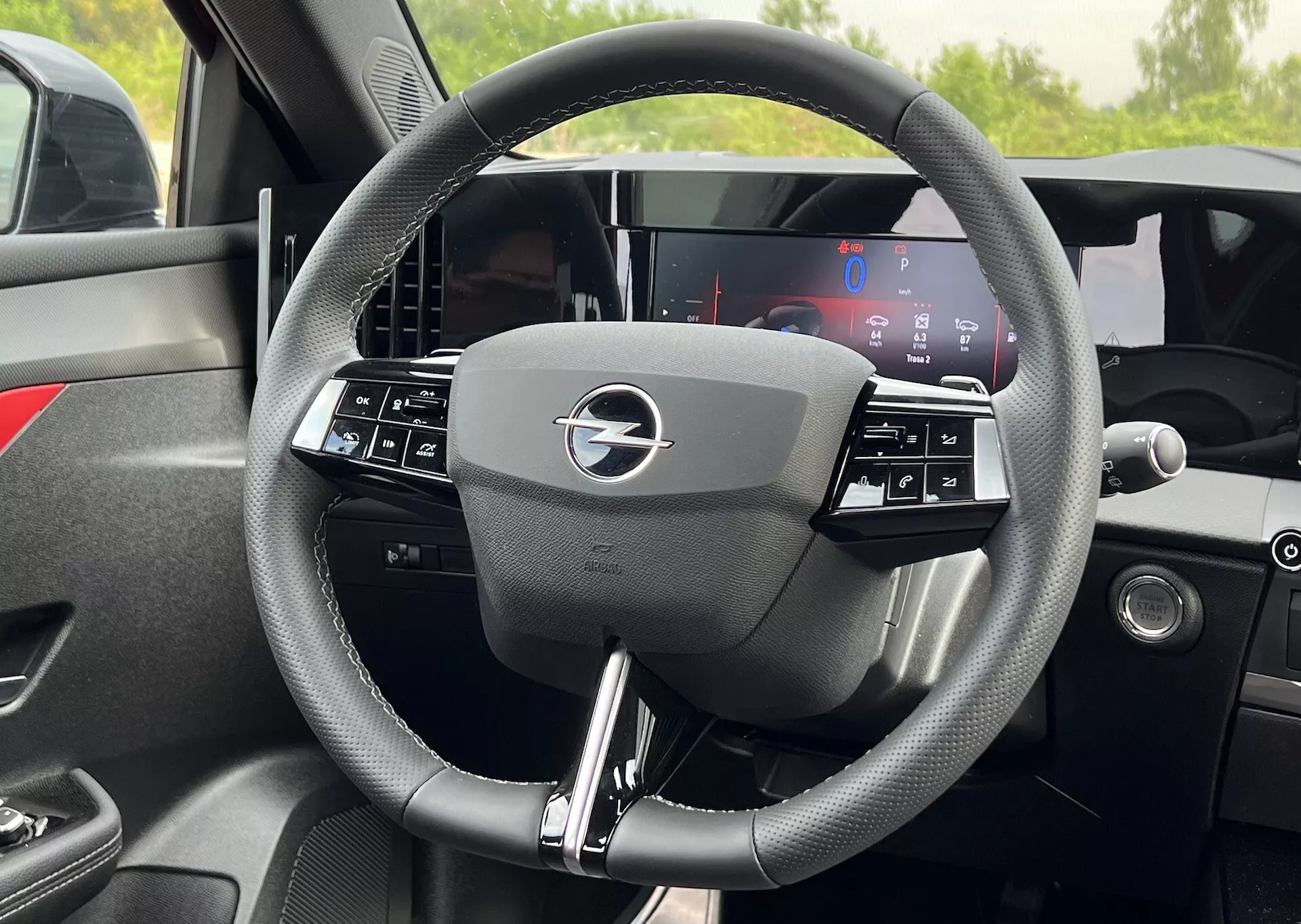 Vista interior detalhada do volante do Opel Astra 2022 com design de três raios com controles integrados e um display de painel totalmente digital atrás, destacando a tecnologia de veículo moderno e ergonomia