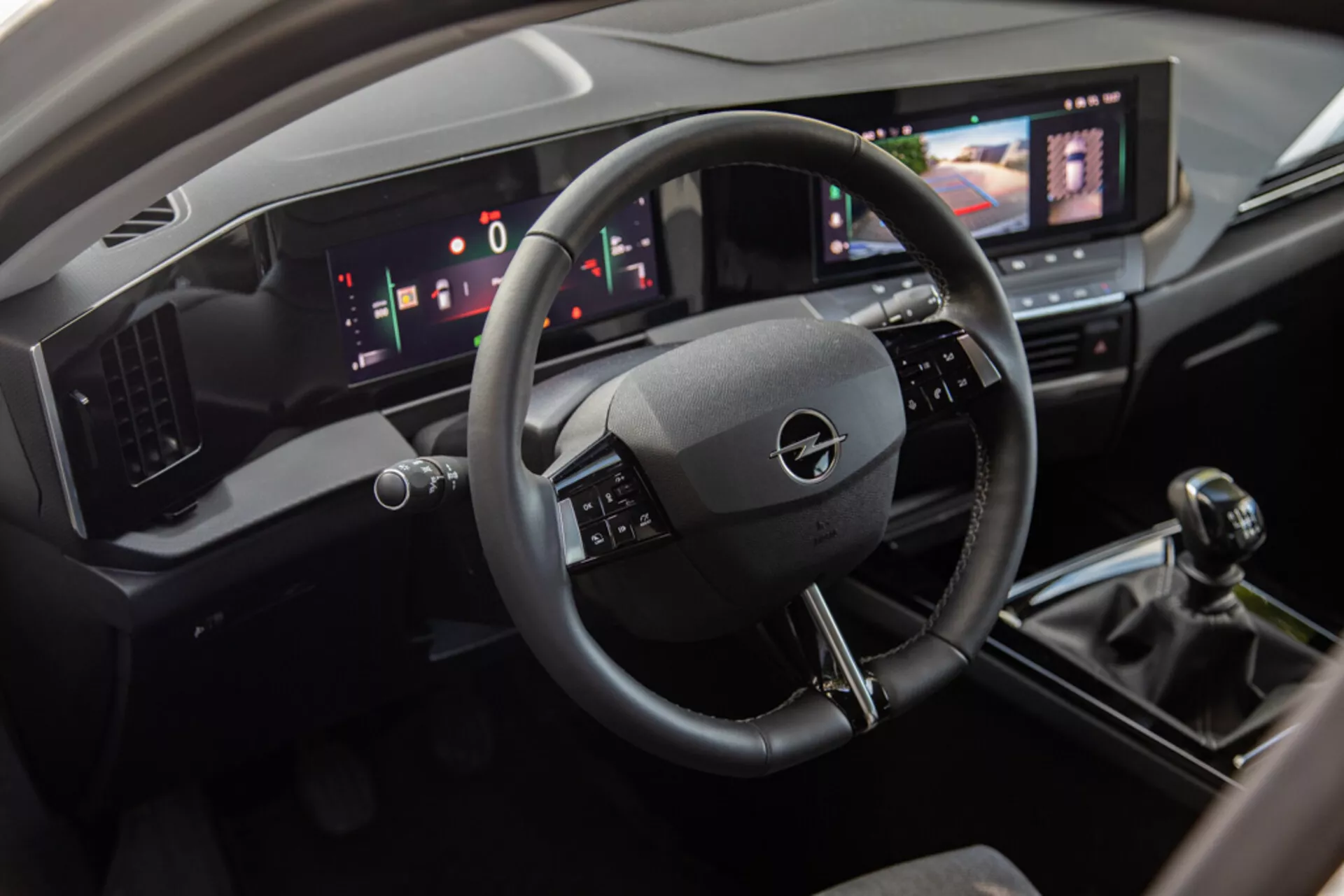 Vista interior do Opel Astra 2022 mostrando a área do motorista com volante de três braços, painel de instrumentos digital e console central incluindo um sistema de infotenimento touchscreen, câmbio manual e controles modernos de climatização