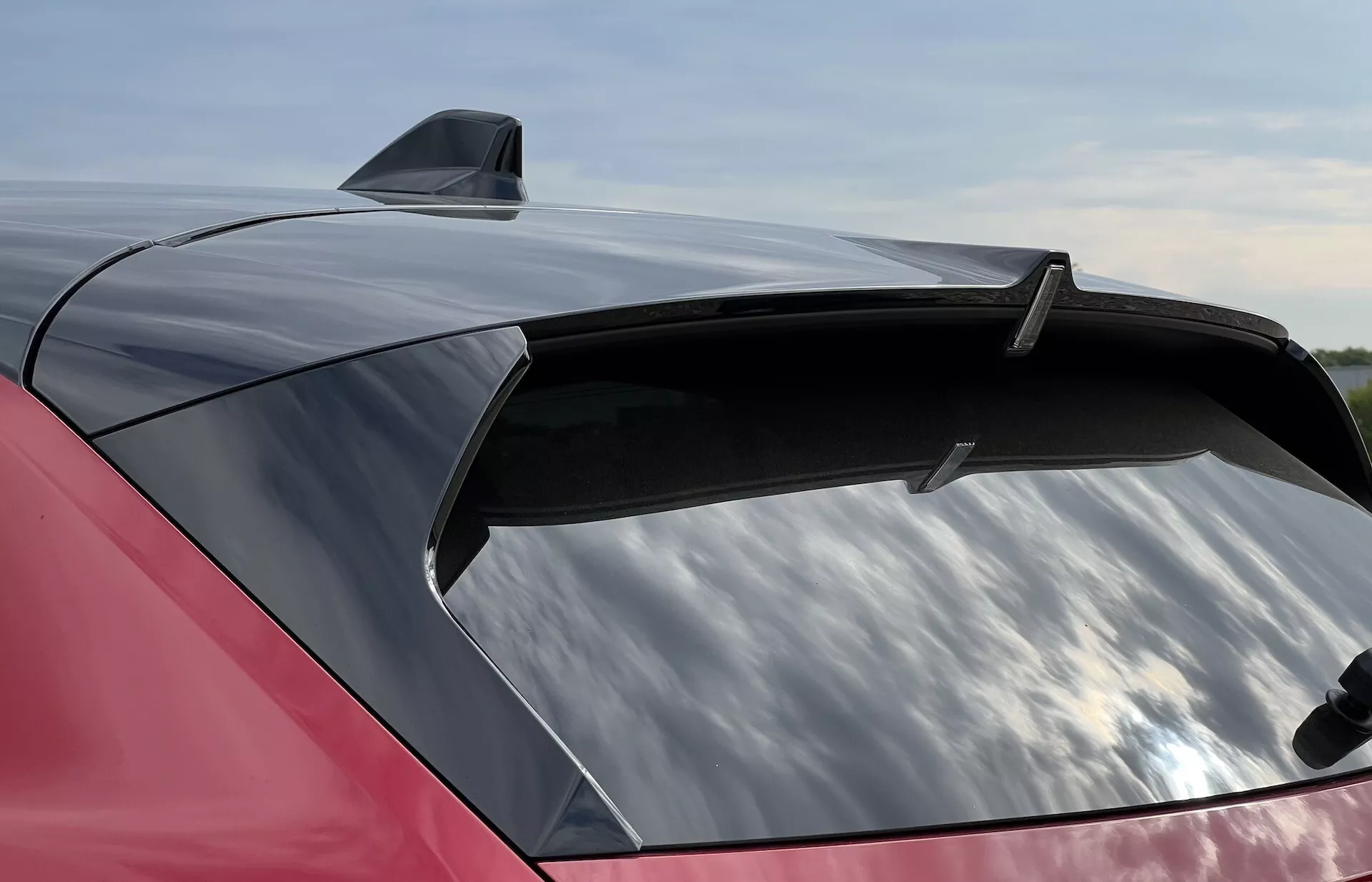 Vista detalhada da secção traseira vermelha brilhante de um Opel Astra 2022 com um spoiler elegante e uma antena de barbatana de tubarão, destacando o grande para-brisa traseiro aerodinâmico com potencial revestimento protetor UV.