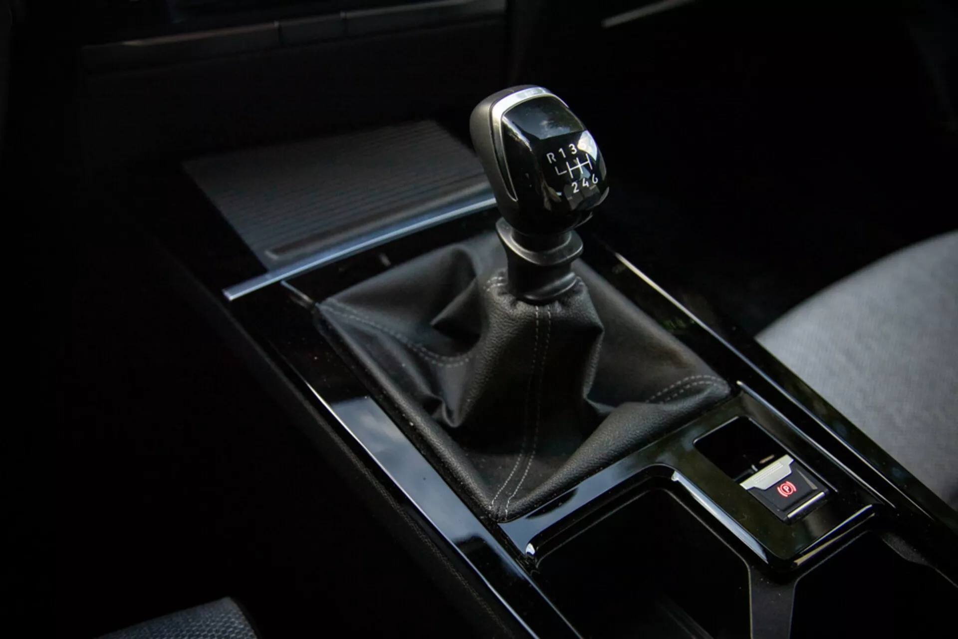 Vista de perto da alavanca de câmbio manual do Opel Astra 2022 no quadrante superior direito com bota de couro, console preto brilhante e elementos interiores ao redor