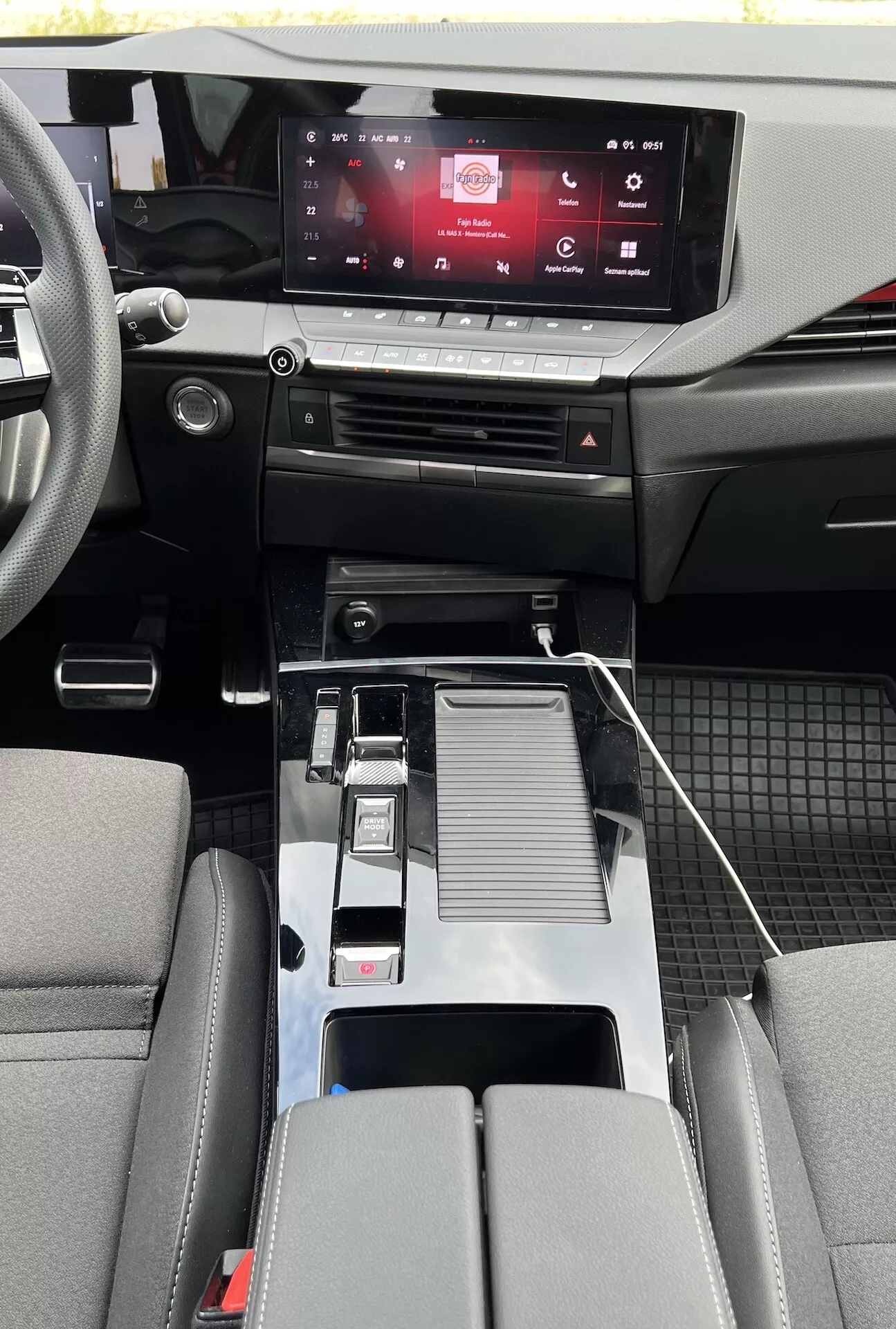 Visão interior do Opel Astra 2022 exibindo design moderno da cabine com sistema de infotainment touchscreen, controles climáticos sensíveis ao toque, alavanca de câmbio metálica, conectividade USB, porta-copos, apoio de braço central detalhado, assentos bicolores e detalhamento de cabine de materiais mistos com tapetes duráveis