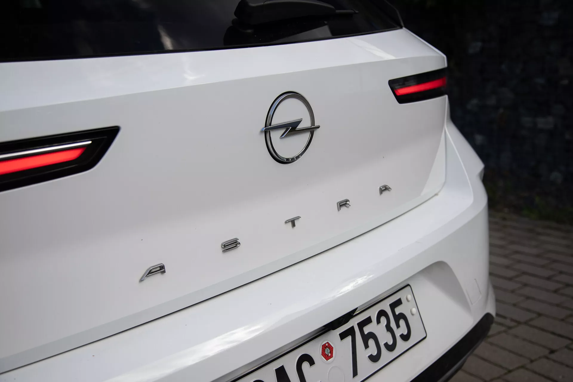 Vista detalhada da parte traseira de um Opel Astra branco de 2022, destacando as luzes traseiras LED, o logotipo da Opel e o nome do modelo 'ASTRA' na tampa do porta-malas