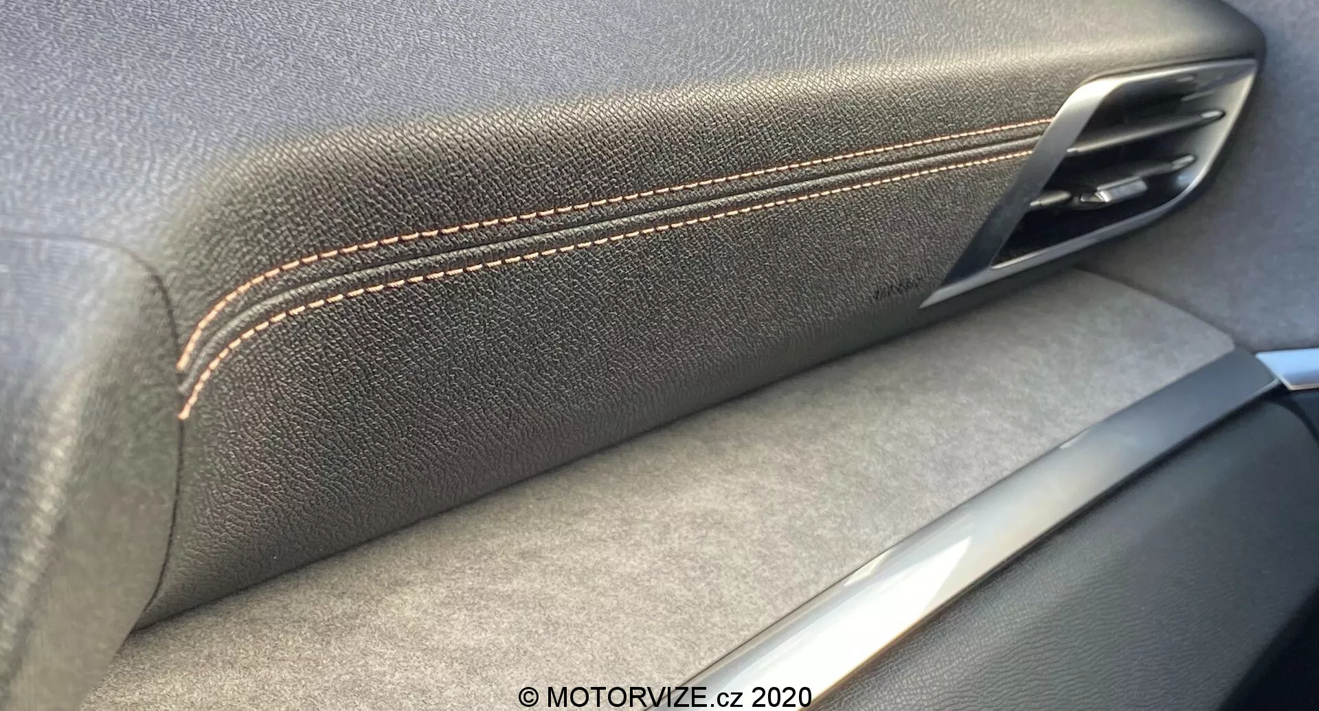 Imagem de close-up do interior do painel da porta do Peugeot 3008 2021, destacando a convergência do apoio de braço texturizado de couro com costura contrastante e o puxador da porta metálico. Os detalhes prateados sugerem um foco na artesania e qualidade dos materiais, com sombras indicando uma fonte de luz interior.