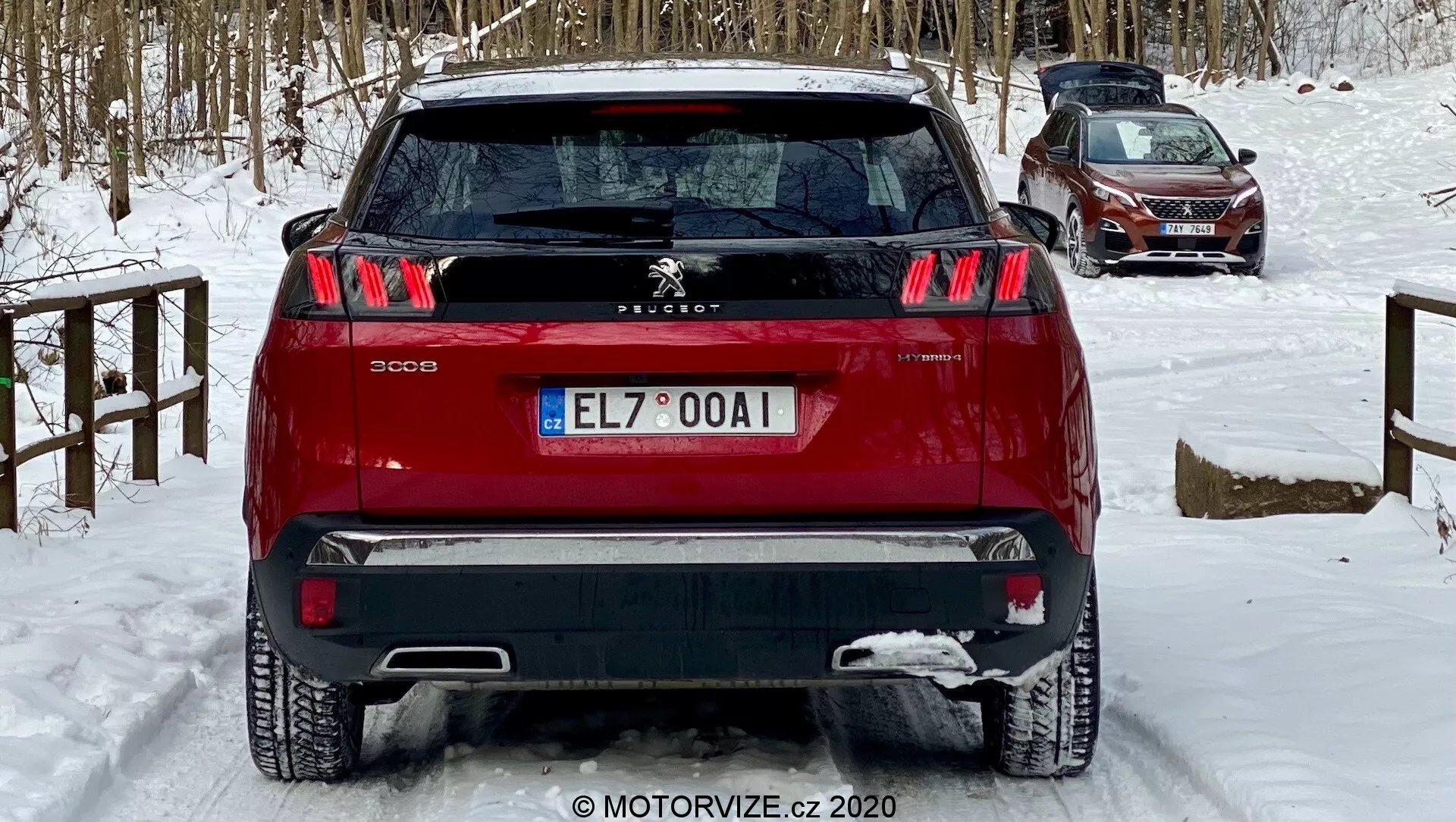 Vista traseira de um SUV Peugeot 3008 vermelho capturada de um ângulo baixo, destacando suas distintas luzes traseiras com design de três garras, emblema central do Leão Peugeot e para-choque de dois tons. O veículo, situado em um terreno coberto de neve, indica condições de inverno. As características visíveis incluem sensores de estacionamento traseiros, limpador do para-brisa traseiro e uma antena traseira superior, sugerindo tecnologia de assistência ao motorista e funcionalidade potencial de GPS/radio, adequado para discussões sobre design automotivo, características de segurança e condução no inverno.
