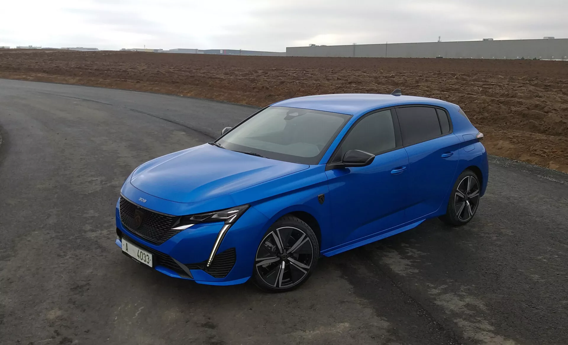 Peugeot 308 hatchback 2022 em azul brilhante, com design aerodinâmico, faróis LED, grade frontal avançada, rodas de liga leve multirraios e características de segurança modernas, estacionado no asfalto