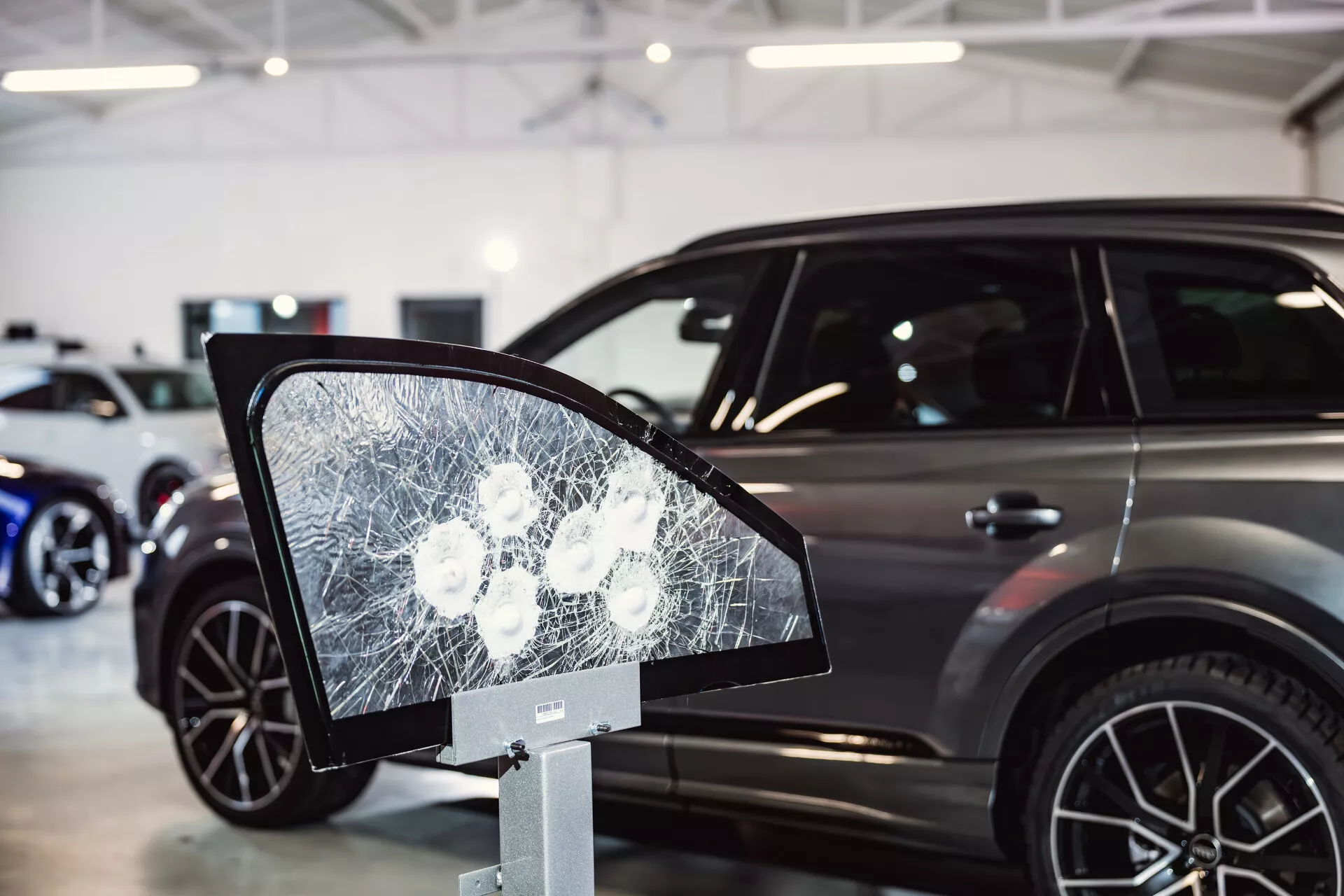 Peugeot 308 2022 em exposição em showroom com foco em display de vidro quebrado que se assemelha a um espelho lateral em primeiro plano, sugerindo características de segurança ou testes de durabilidade, e apresentando o perfil lateral elegante do carro com características de SUV moderno ao fundo