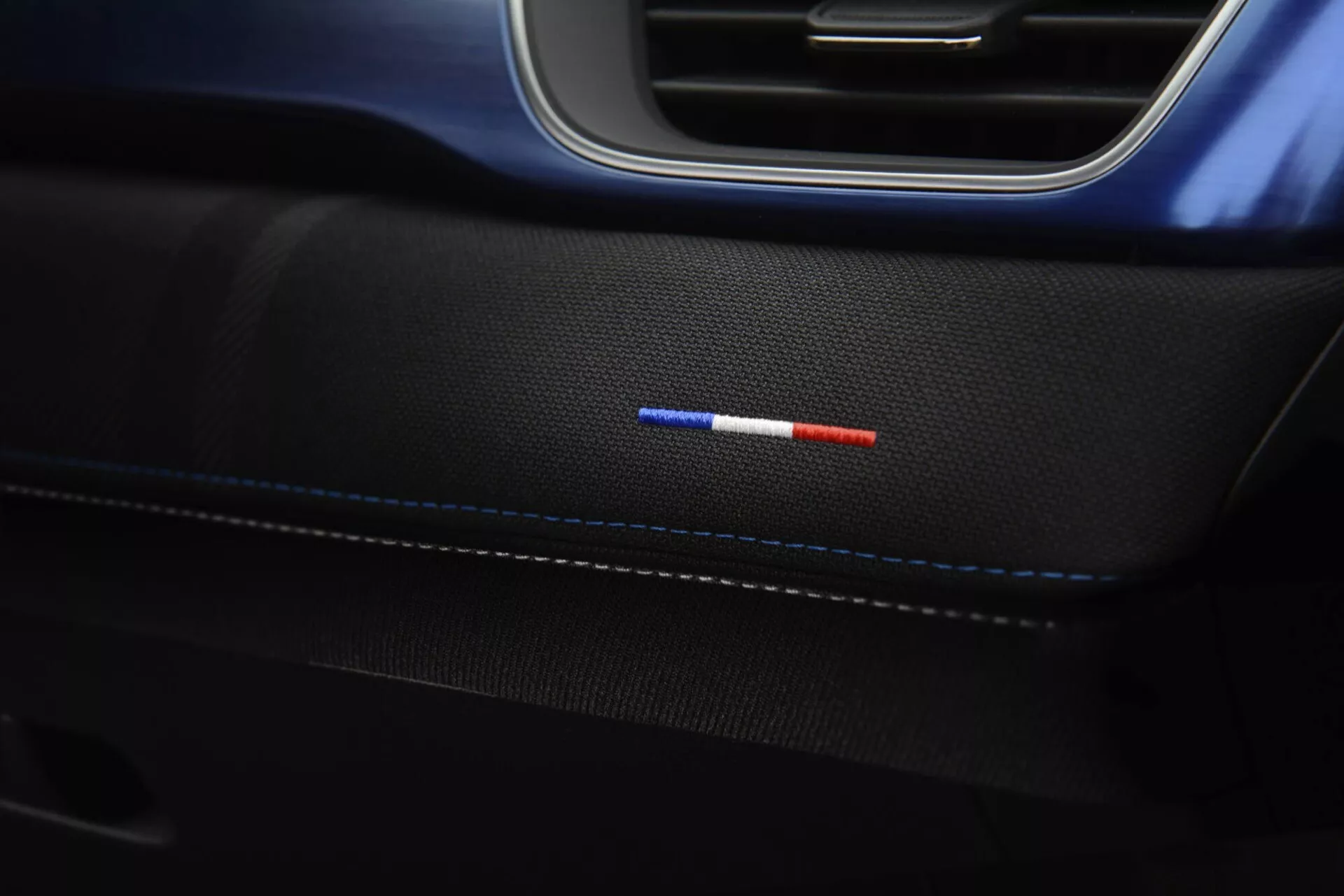 Fotografia detalhada do painel da porta interior do Renault Captur 2024 com costura sutil em couro preto de alta qualidade, iluminação ambiente em dois tons de vermelho e azul, e acabamento elegante em preto e azul, exibindo detalhes de design elegante e tecnologia de iluminação avançada
