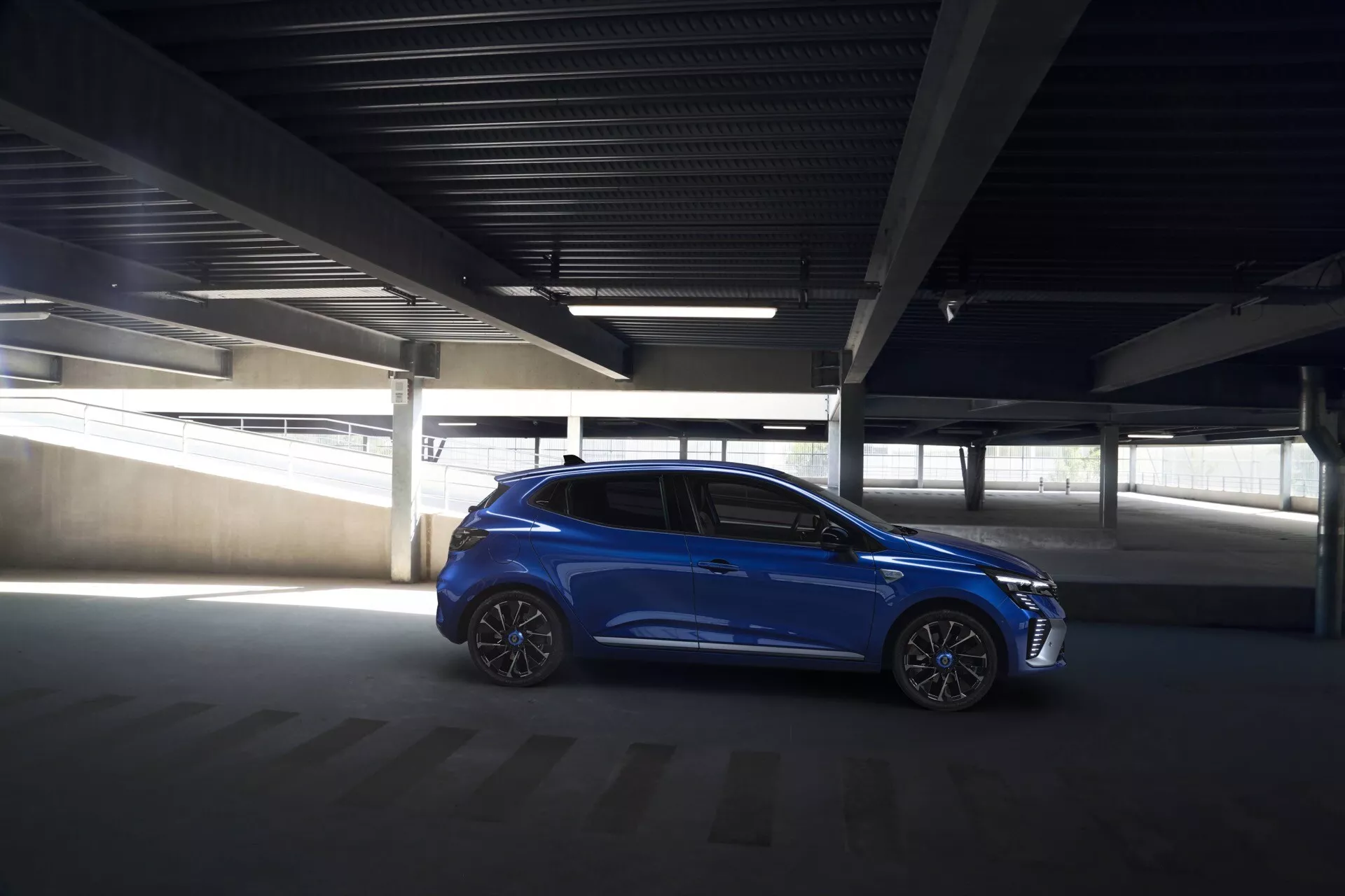 Hatchback azul Renault Clio V-facelift 2023 estacionado em ângulo em um estacionamento pouco iluminado, destacando seu design elegante, rodas de liga e recursos tecnológicos integrados