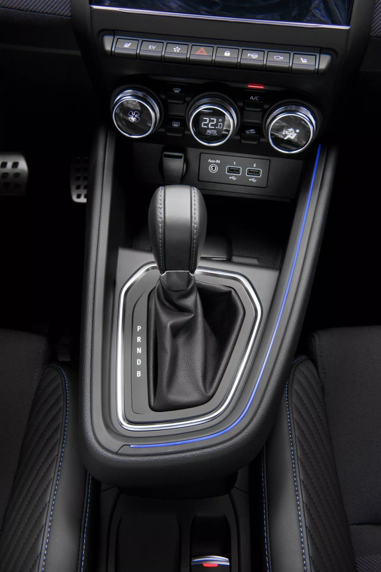 Visão superior do console central do Renault Clio V-Facelift 2023 com alavanca de câmbio na posição Park, acabamentos em prata, costuras em couro preto, controles de climatização e sistema de ignição sem chave