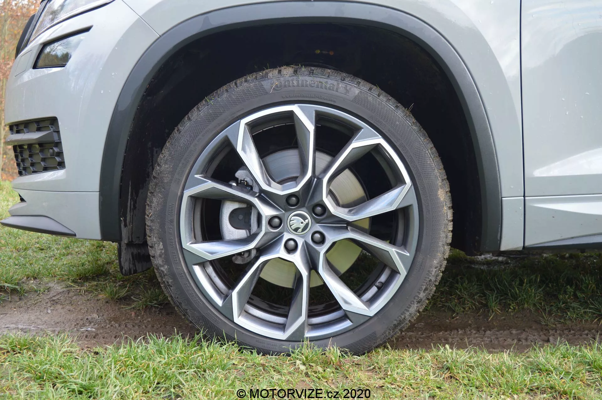 Imagem em close da roda dianteira do lado do passageiro de um Skoda Kodiaq 2017, destacando seu moderno design de roda de liga leve com múltiplos raios e acabamentos pintados e usinados. A roda de liga apresenta dez raios em cores metálicas escuras contrastantes e mais claras, projetada tanto para apelo estético quanto para proteção contra a calçada. A imagem também destaca o pneu de todas as estações ou todo-o-terreno com desenho visível do piso e um design de proteção da borda da roda, e mostra parcialmente a cor da carroceria prata metálica ou cinza clara junto com um elemento de acabamento plástico ao redor do arco das rodas, aludindo à estética robusta e capaz fora de estrada do SUV.