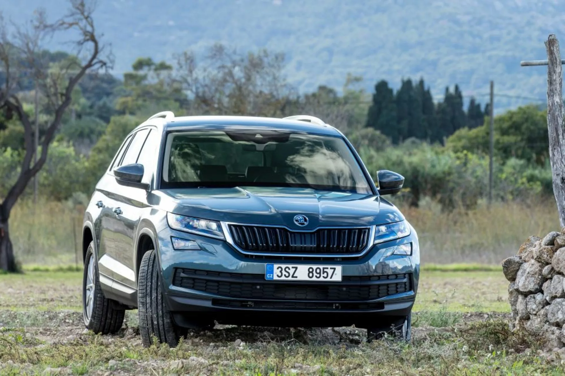 Skoda Kodiaq de 2017 em uma vista frontal e lateral dinâmica mostrando faróis LED, luzes de condução diurna, grade frontal com ripas verticais, rodas de liga leve de múltiplos raios, proteção de carroceria e acabamentos laterais, espelhos laterais com indicadores de direção e janelas com pelicula, ambientado em um terreno natural propício para condução off-road
