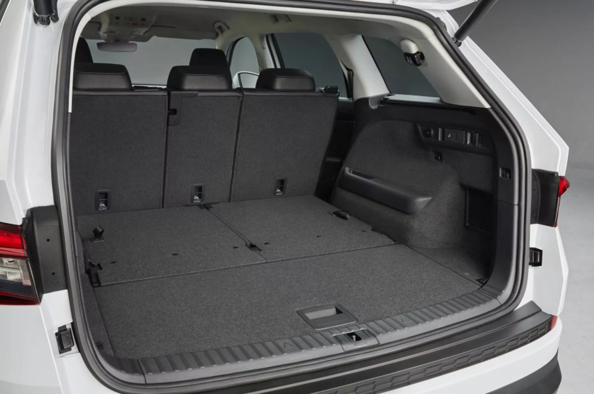 Vista do espaço de carga traseiro Skoda Kodiaq 2017 com a porta da bagageira aberta, apresentando uma área de carga alcatifada vazia, bancos traseiros rebatíveis para espaço ampliado, acabamento lateral em plástico com compartimento de arrumação embutido, pontos de fixação e iluminação interior, destacando soluções práticas para armazenamento e gestão de carga.