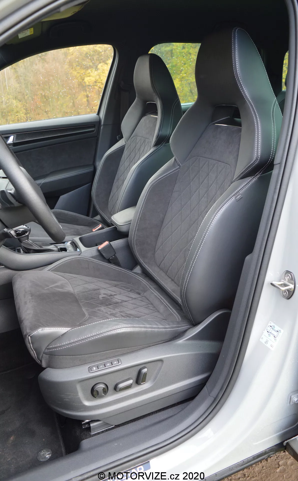 Vista interior de um Skoda Kodiaq 2017 focando no assento do motorista e sua área circundante, com estofamento de couro preto com costura em diamante, apoio de cabeça integrado, suporte lateral para condução dinâmica e ajustes eletrônicos do assento com botões de controle. Os recursos visíveis incluem o quadro inferior da porta com placa de soleira e unidade de alto-falante, indicativos de um interior luxuoso e esportivo com tecnologia avançada de assento.