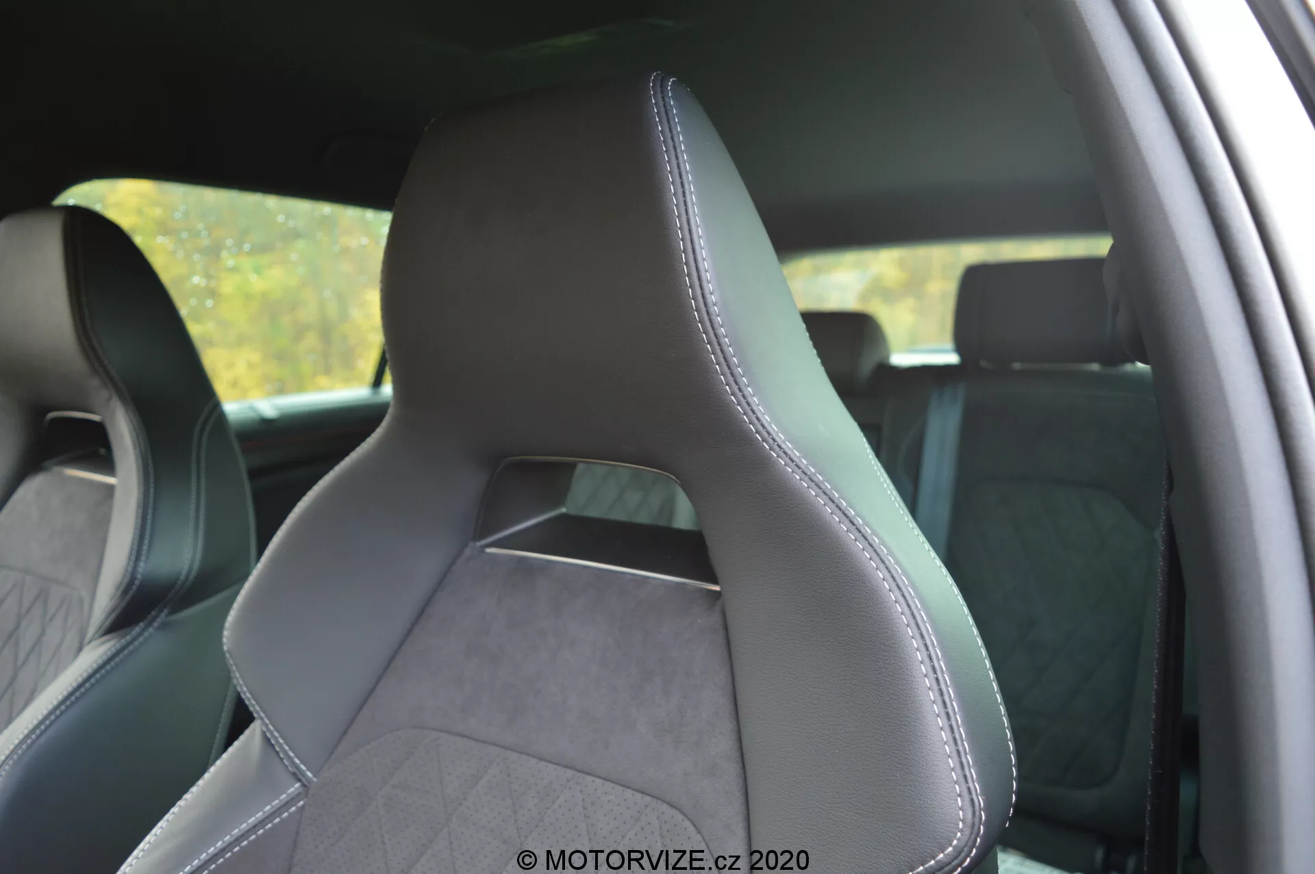 Interior de um Škoda Kodiaq 2017 focando no banco do motorista dianteiro a partir de uma perspectiva lateral traseira, destacando o estofamento em couro e tecido texturizado com costuras precisas ao longo das bordas. O assento de design moderno e esportivo possui abas laterais pronunciadas para um suporte aprimorado, encosto de cabeça integrado e padrão de costura em diamante que sugere uma estética premium. O fundo do interior está ligeiramente desfocado para enfatizar o assento.