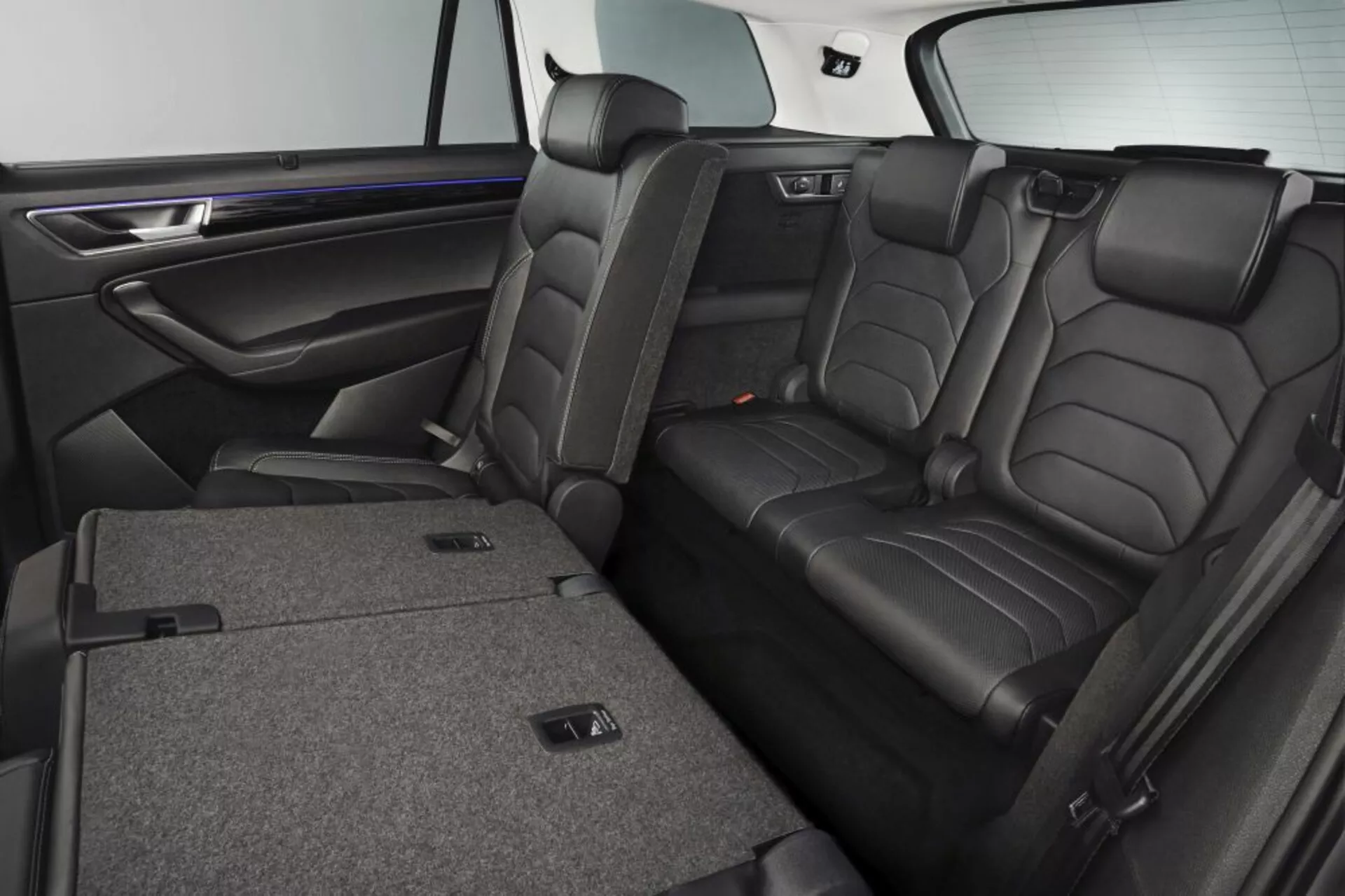 Interior do Skoda Kodiaq 2017 exibindo assentos traseiros de couro de luxo com apoios de cabeça, recursos de dobramento 60/40 para expansão do espaço de carga, apoio de braço central com porta-copos, e acabamento de porta com efeito de madeira premium e iluminação ambiente