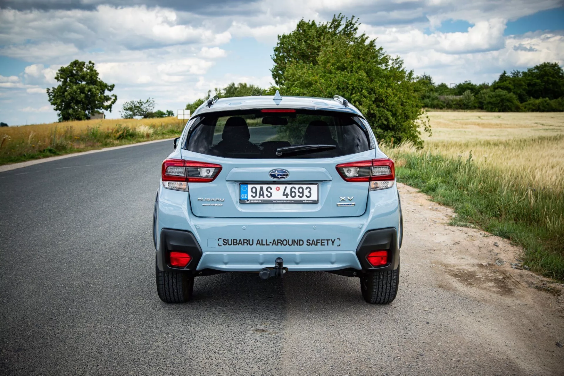 Vista traseira de um Subaru XV 2021 em uma estrada rural, mostrando as luzes traseiras distintivas do carro, sistema de escape duplo e tampa do porta-malas com etiqueta de segurança sob um céu parcialmente nublado