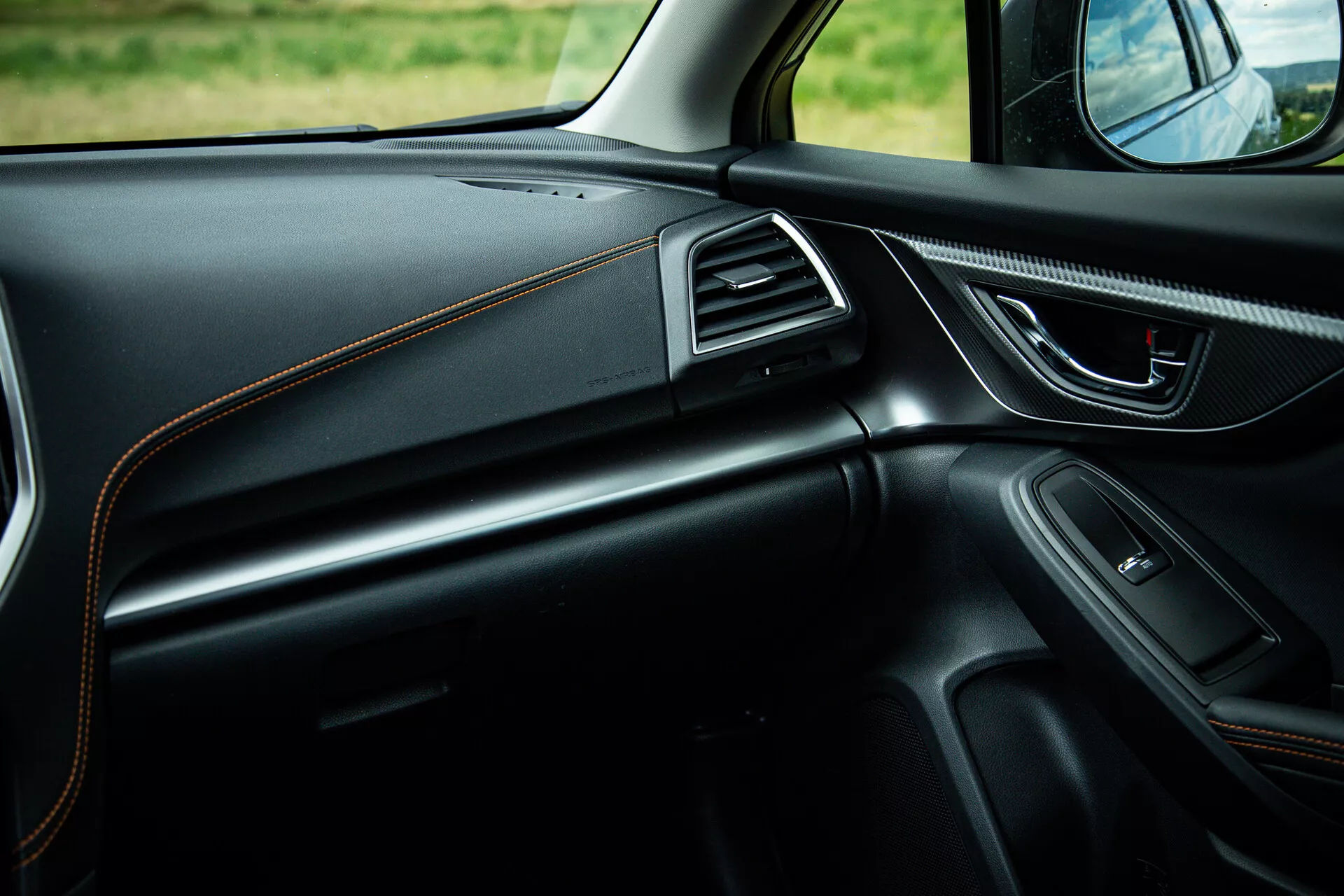 Vista do interior da Subaru XV 2021 focando no lado do passageiro mostrando design elegante do painel com costura contrastante, maçaneta da porta ergonômica com controles de potência, alto-falante integrado, entradas de ar com contorno em cromo e iluminação ambiente