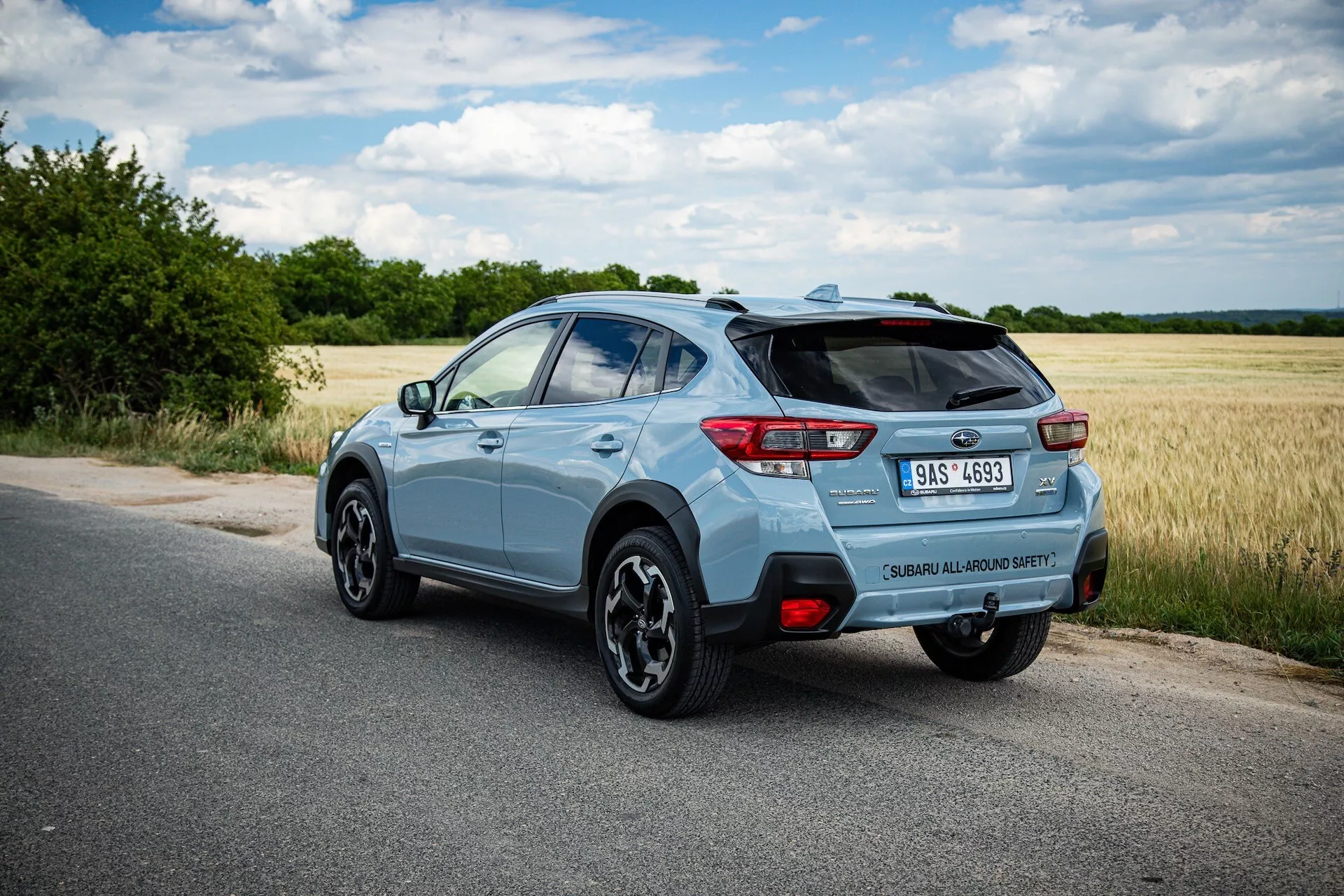 SUV compacto Subaru XV azul claro 2021 fotografado de um ângulo traseiro de três quartos destacando o lado direito, postura dinâmica em estrada pavimentada com visão clara do spoiler traseiro, rodas de liga, luzes traseiras LED, emblema do modelo, ponta de escape única e potenciais características tecnológicas