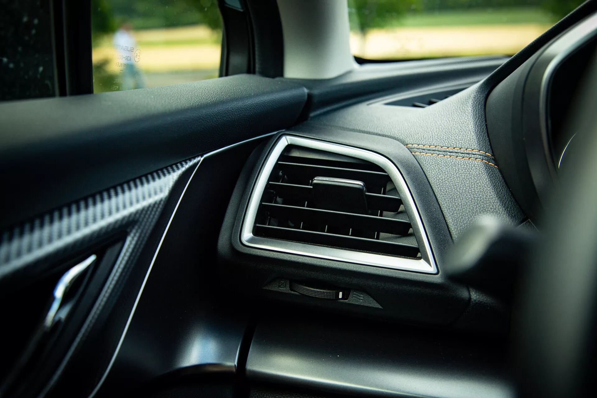 Detalhe do interior do Subaru XV 2021 mostrando o painel do lado do passageiro com saída de ar acentuada em cromo, revestimento em couro preto de qualidade com costuras visíveis e materiais suaves ao toque, fotografado em um ângulo de 45 graus destacando elementos de design moderno à luz natural do dia