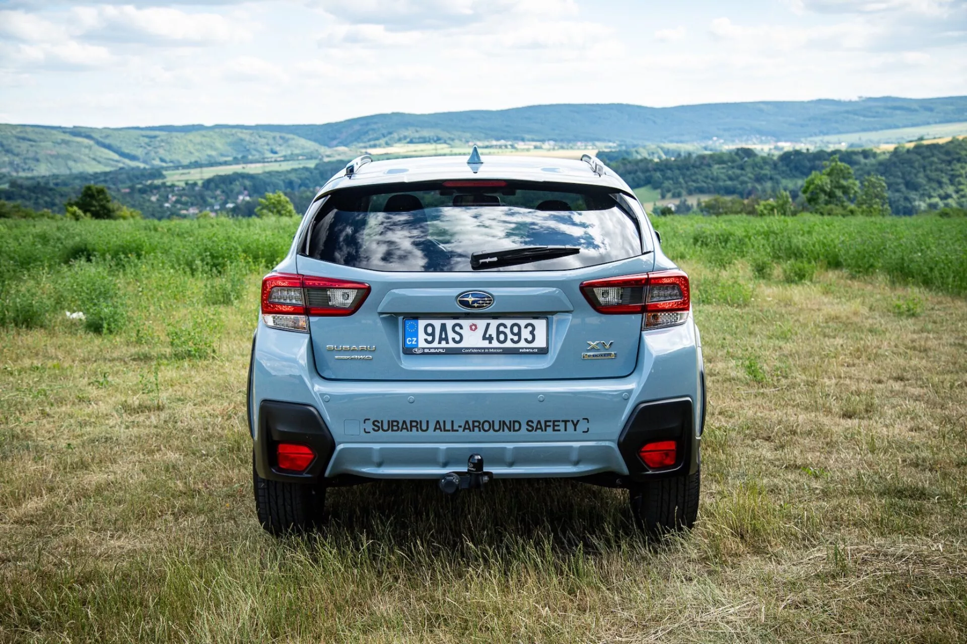 Vista traseira do ângulo do Subaru XV 2021 ao ar livre em um campo com fundo montanhoso, destacando características de segurança e elementos de design moderno de SUV como spoiler traseiro e luzes traseiras ousadas
