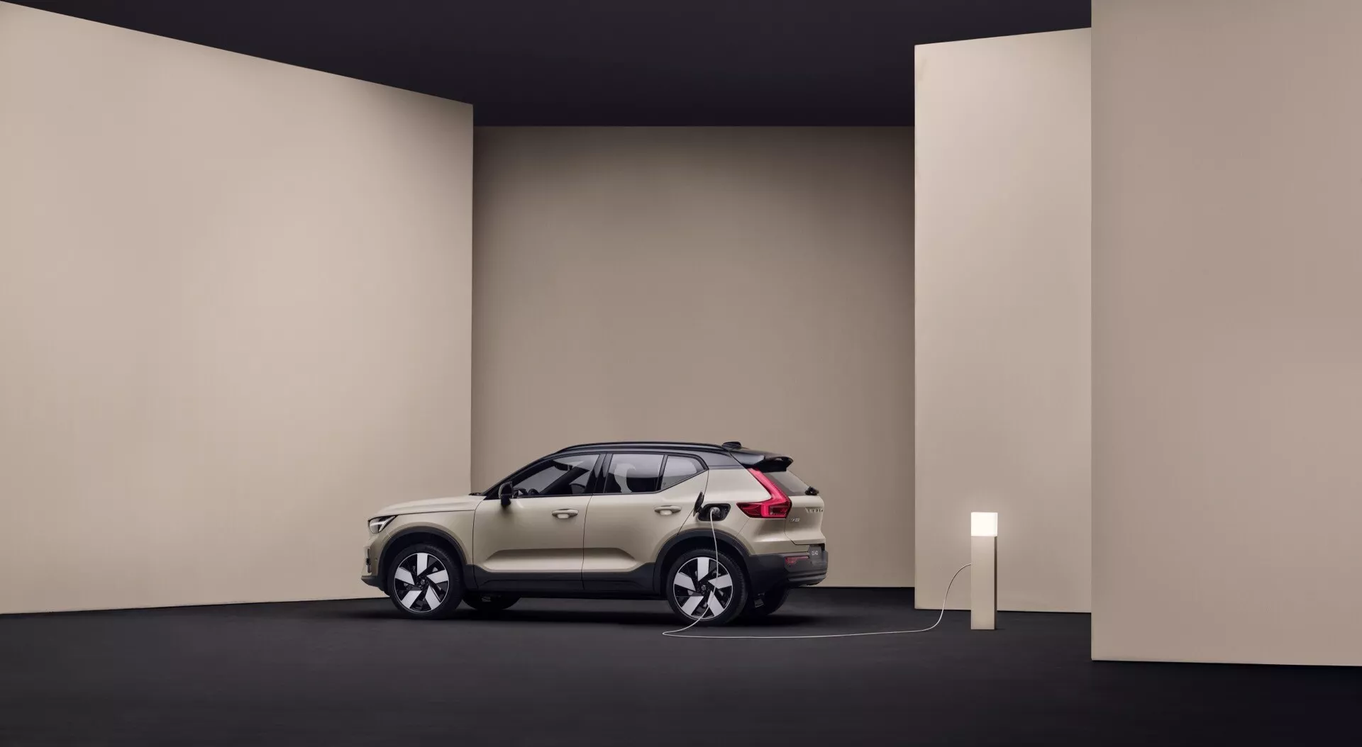 Volvo EX40 1ª geração 2024 em ambiente de estúdio mostrando seu design elegante, cor branca ou prata, conectado a uma estação de carga indicando características de veículo elétrico, posicionado para exibir o perfil e a parte frontal do carro