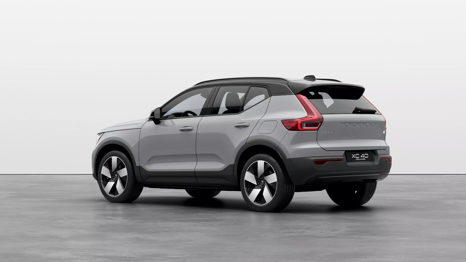 Volvo EX40 primeira geração 2024 em vista traseira de três quartos exibindo sua carroceria SUV compacta a média, linha de teto inclinada esportiva, spoiler traseiro integrado, luzes traseiras LED com assinatura de luz moderna, pontas de escapamento duplas, rodas de liga leve multi-raios e espelhos laterais com setas integradas em um ambiente de estúdio.