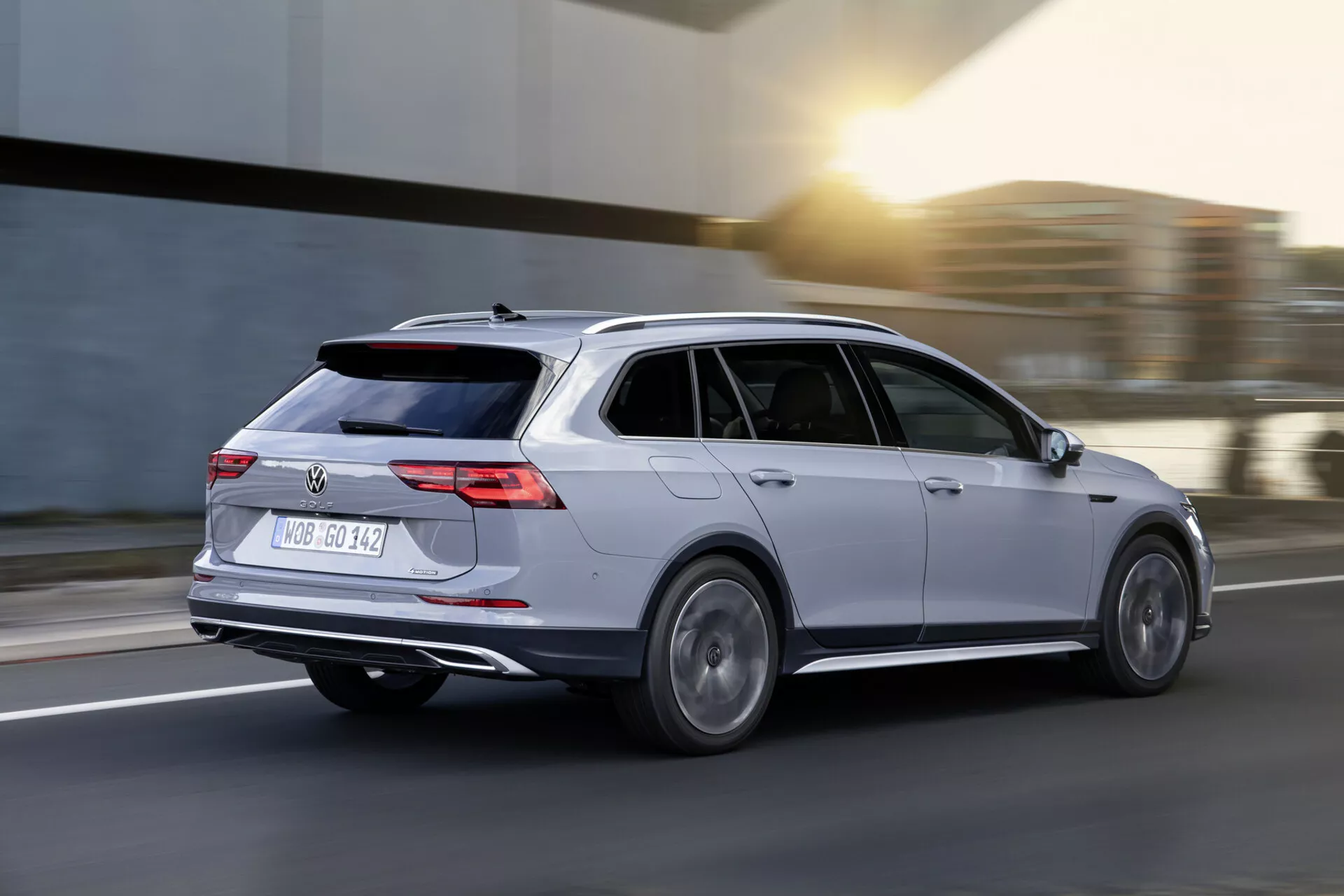 Carrinha Volkswagen Golf Alltrack 2017 em movimento, captada numa vista dinâmica traseira de três quartos destacando a carroçaria prateada, luzes traseiras LED, jantes de liga leve e design aerodinâmico contra um fundo de estrada desfocado.